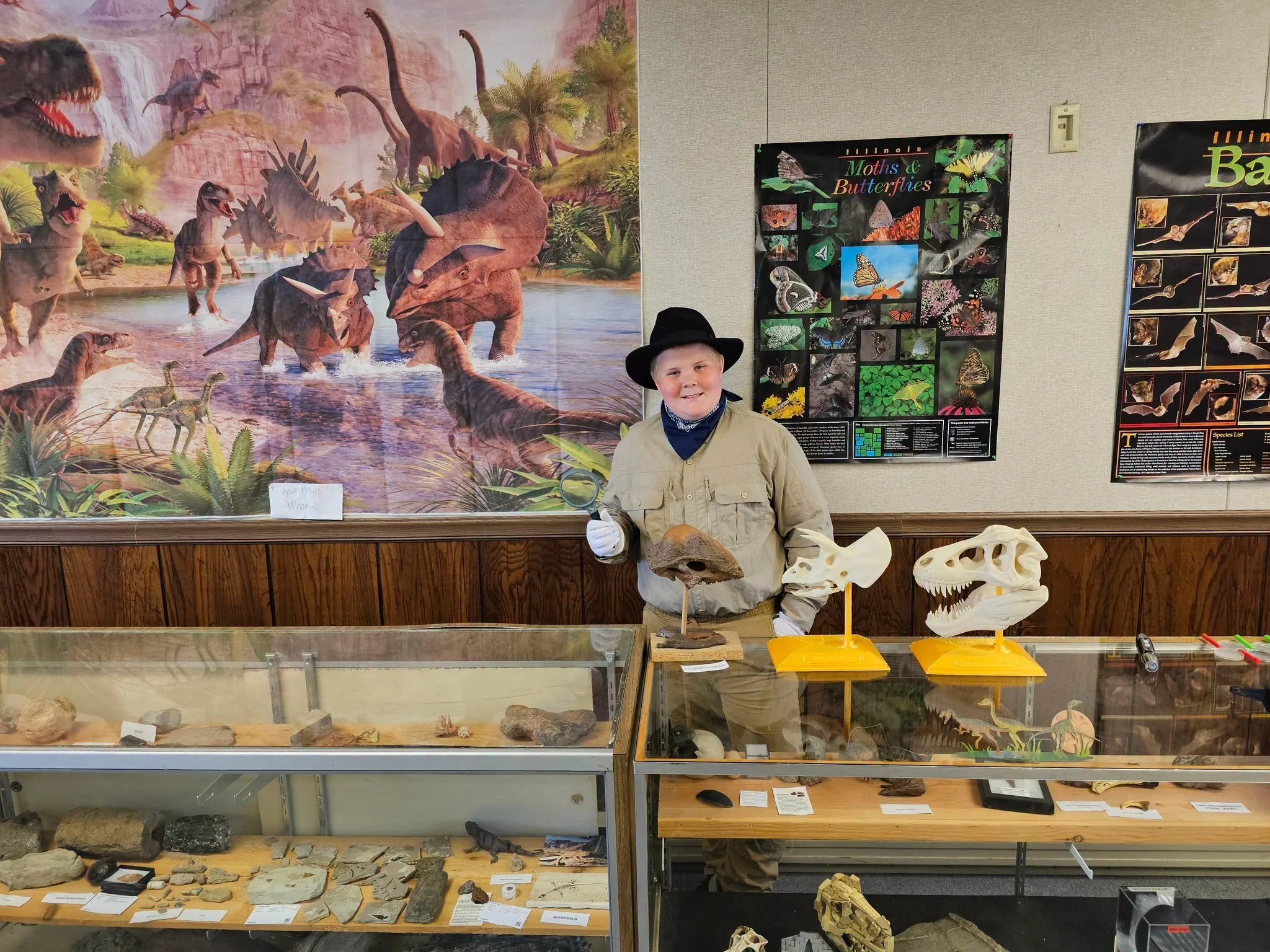 Anderson Taylor in an explorer outfit holding fossil specimens beside museum exhibits.