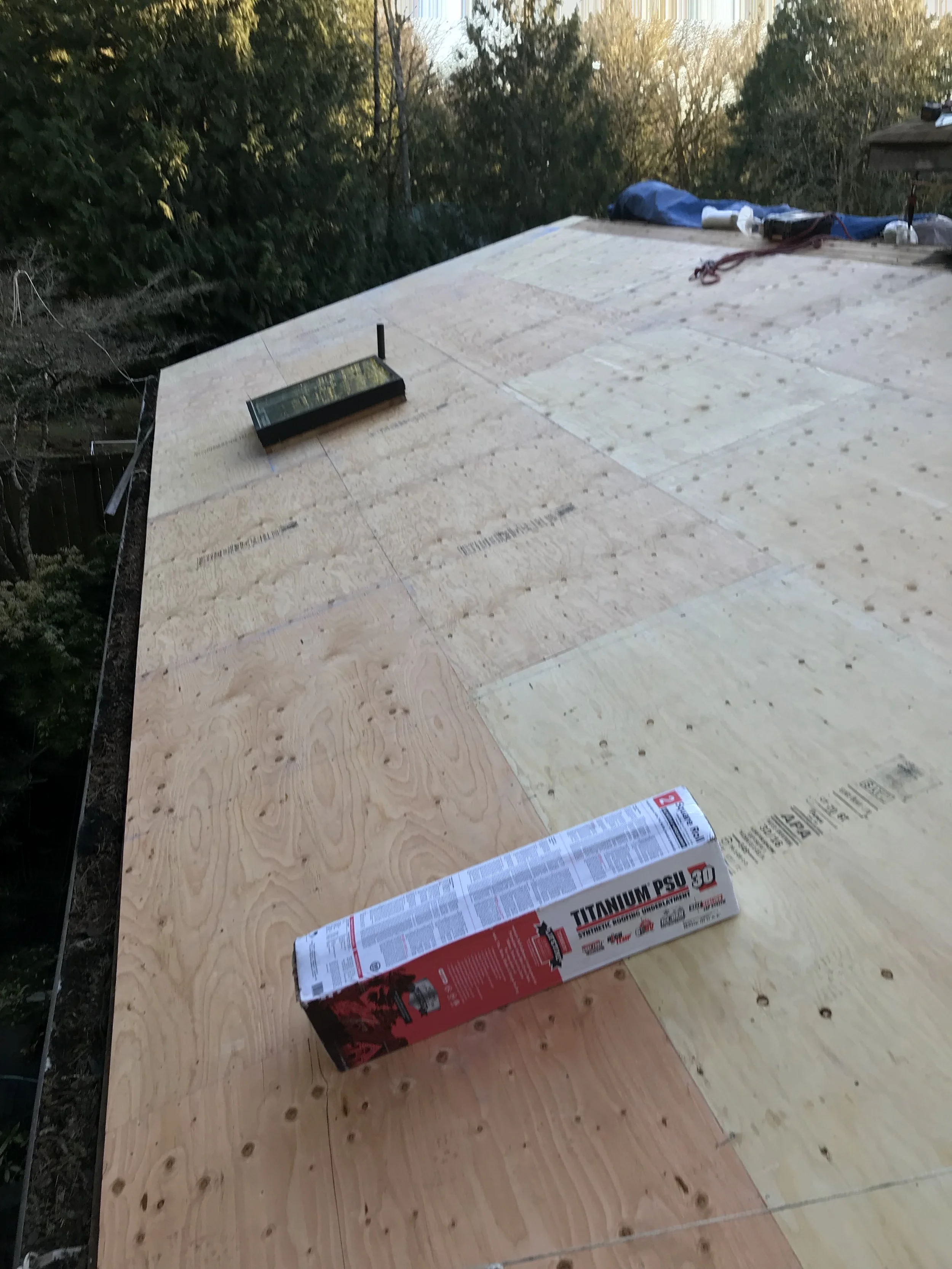 Wooden roof sheathing with a box of titanium PSU insulation and some construction tools and supplies in the background.