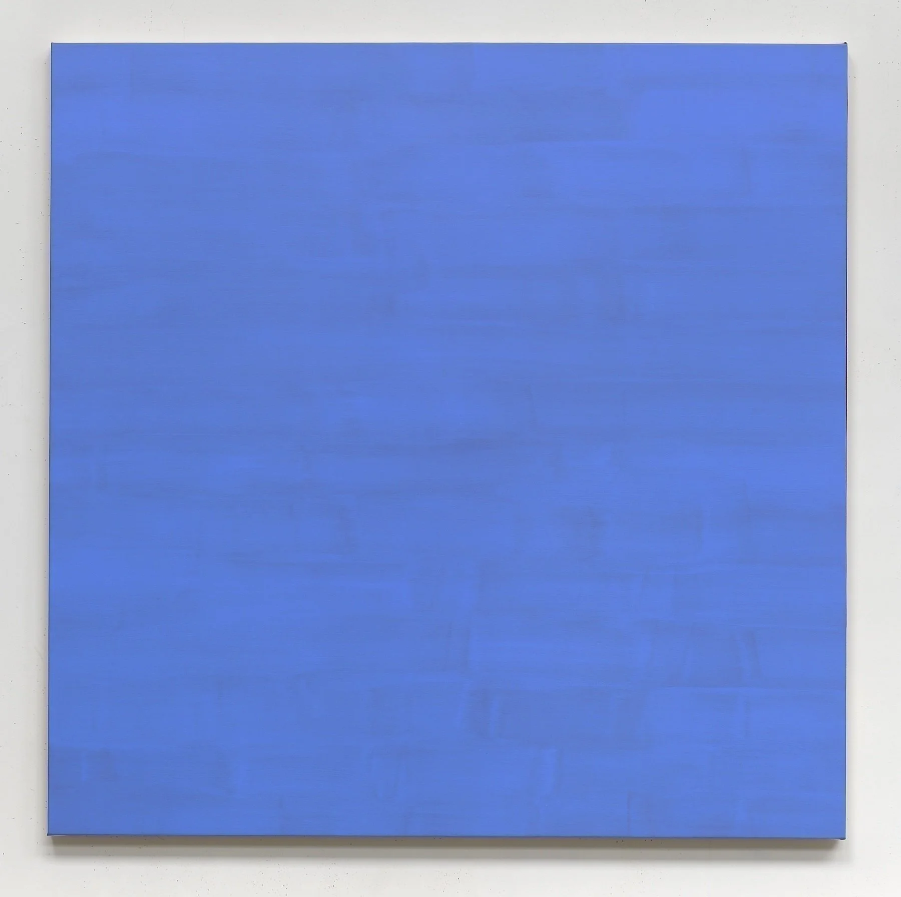 A plain blue square canvas or board mounted on a white wall.