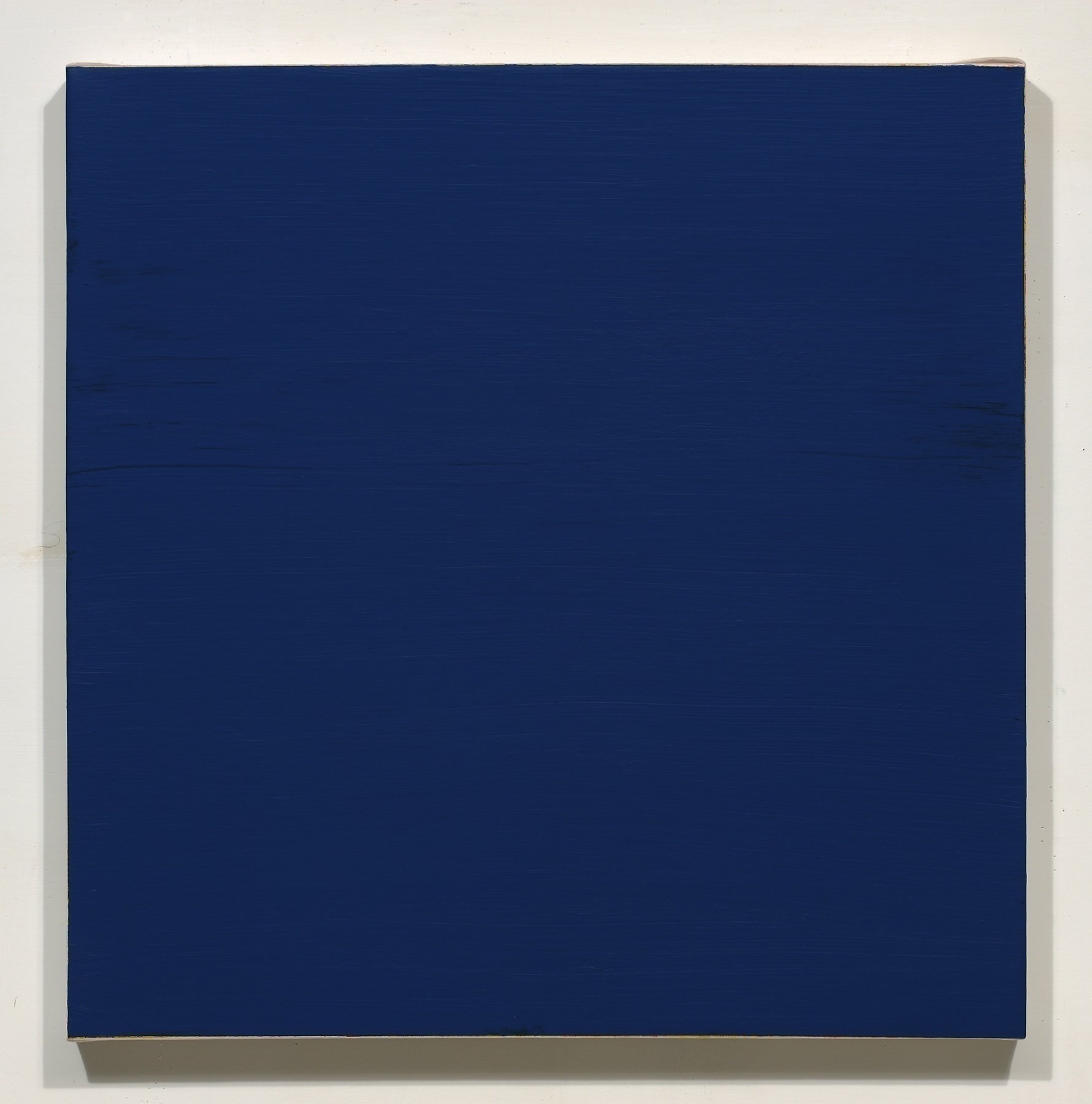 A large, square piece of art with a solid dark blue color, mounted on a white wall.
