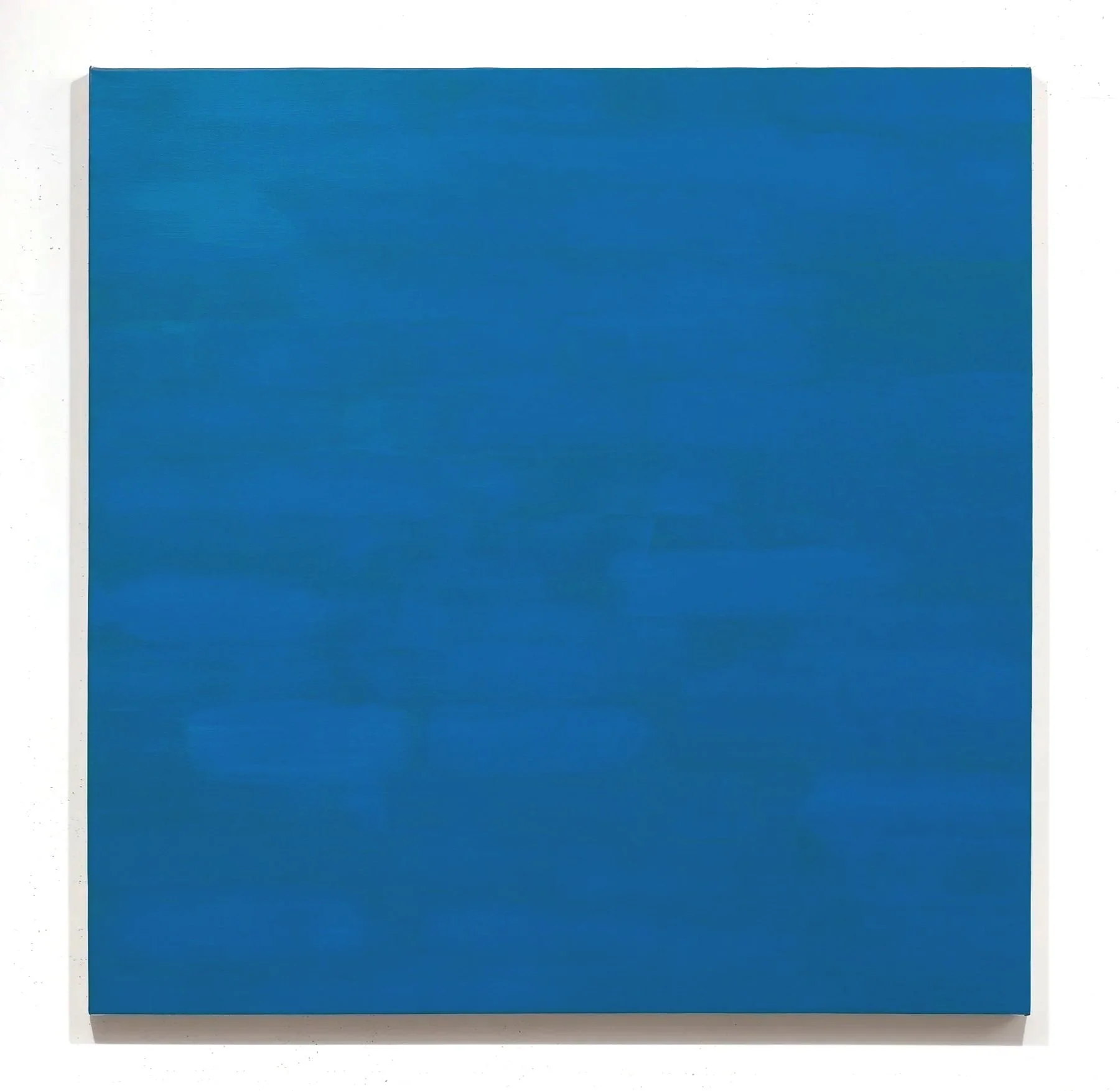 A large rectangular canvas painted in solid blue color hanging on a white wall.