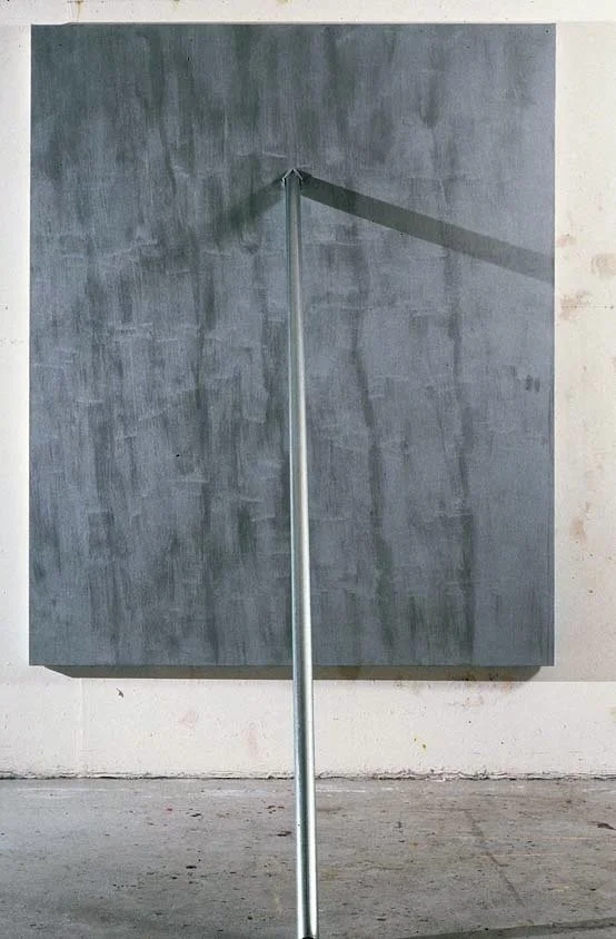 Concrete wall with a metal pole casting a shadow on it, positioned in front of the wall.