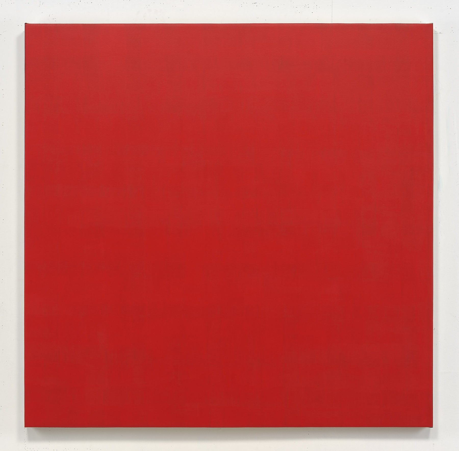 A large red square with a slight texture, mounted on a white wall.