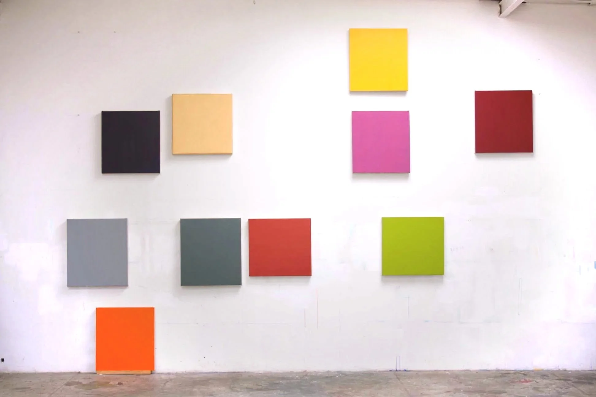 Various colored squares and rectangles arranged on a white gallery wall, including yellow, pink, red, black, coral, gray, green, and orange blocks.