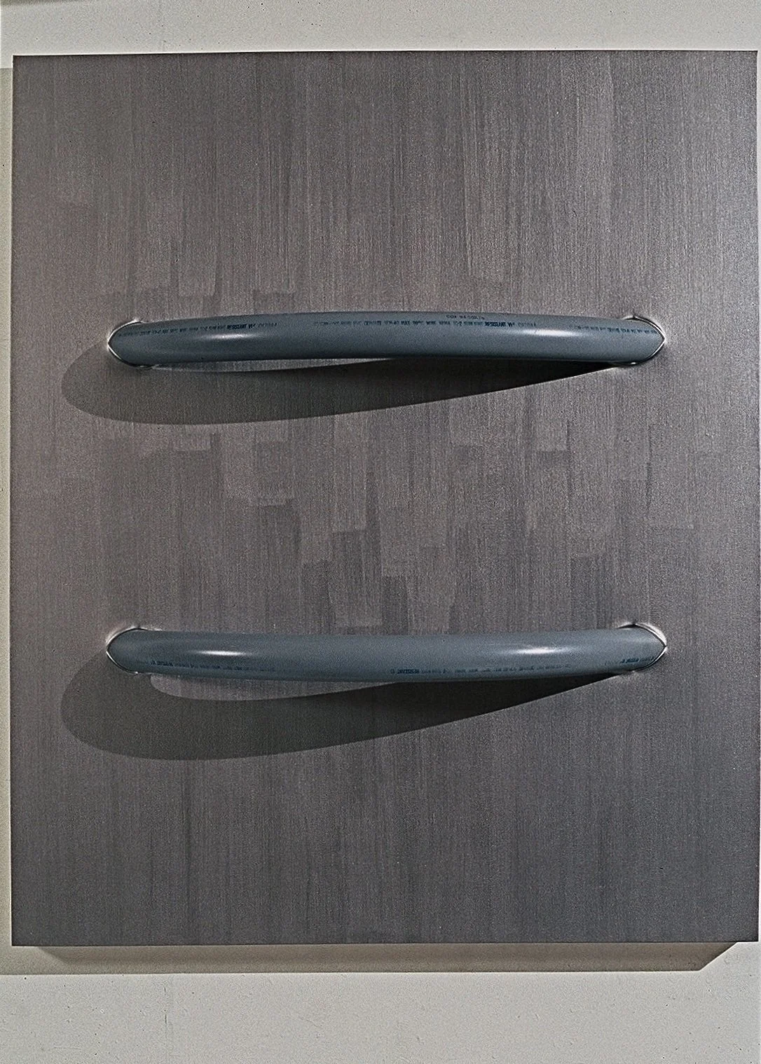 Two silver handles on a textured grey metallic surface, casting shadows.