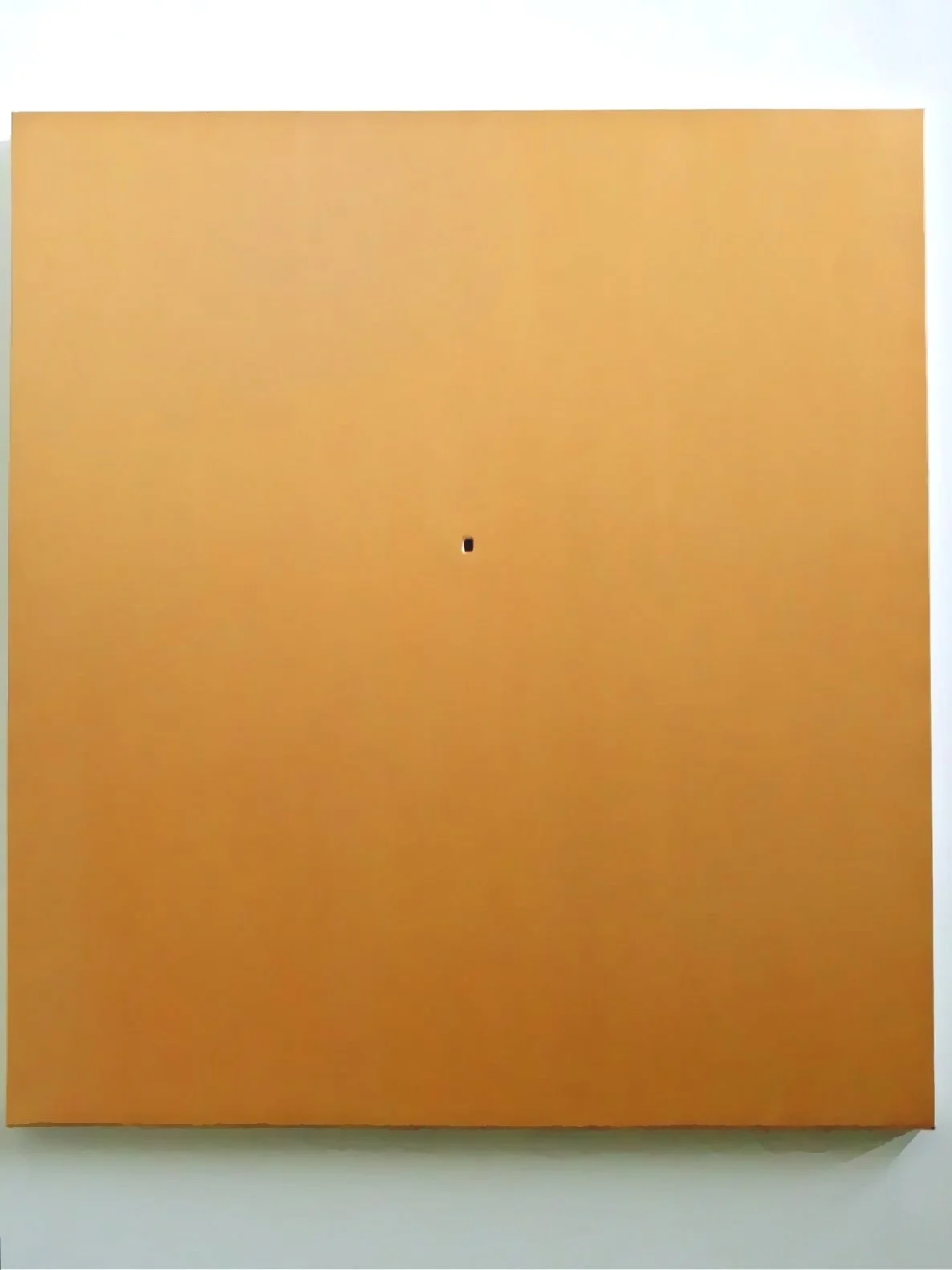 Orange wall or panel with a small black and white rectangular object or hole near the center.