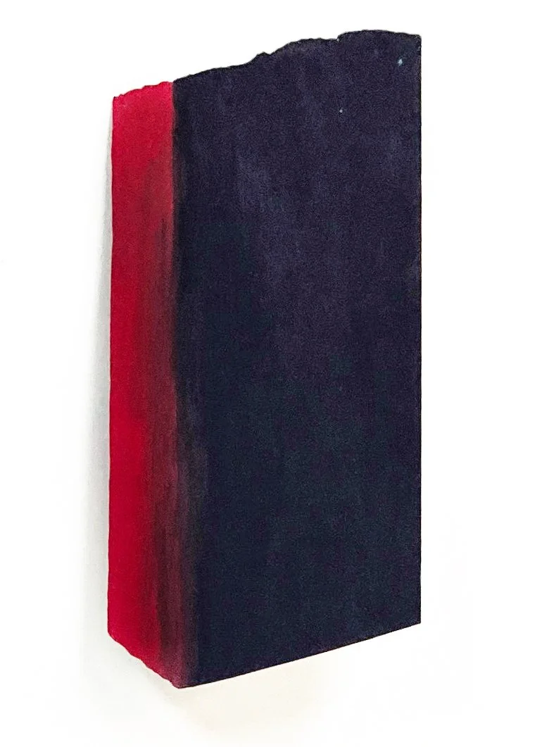 A rectangular black sculpture with a red side edge, mounted on a white background.