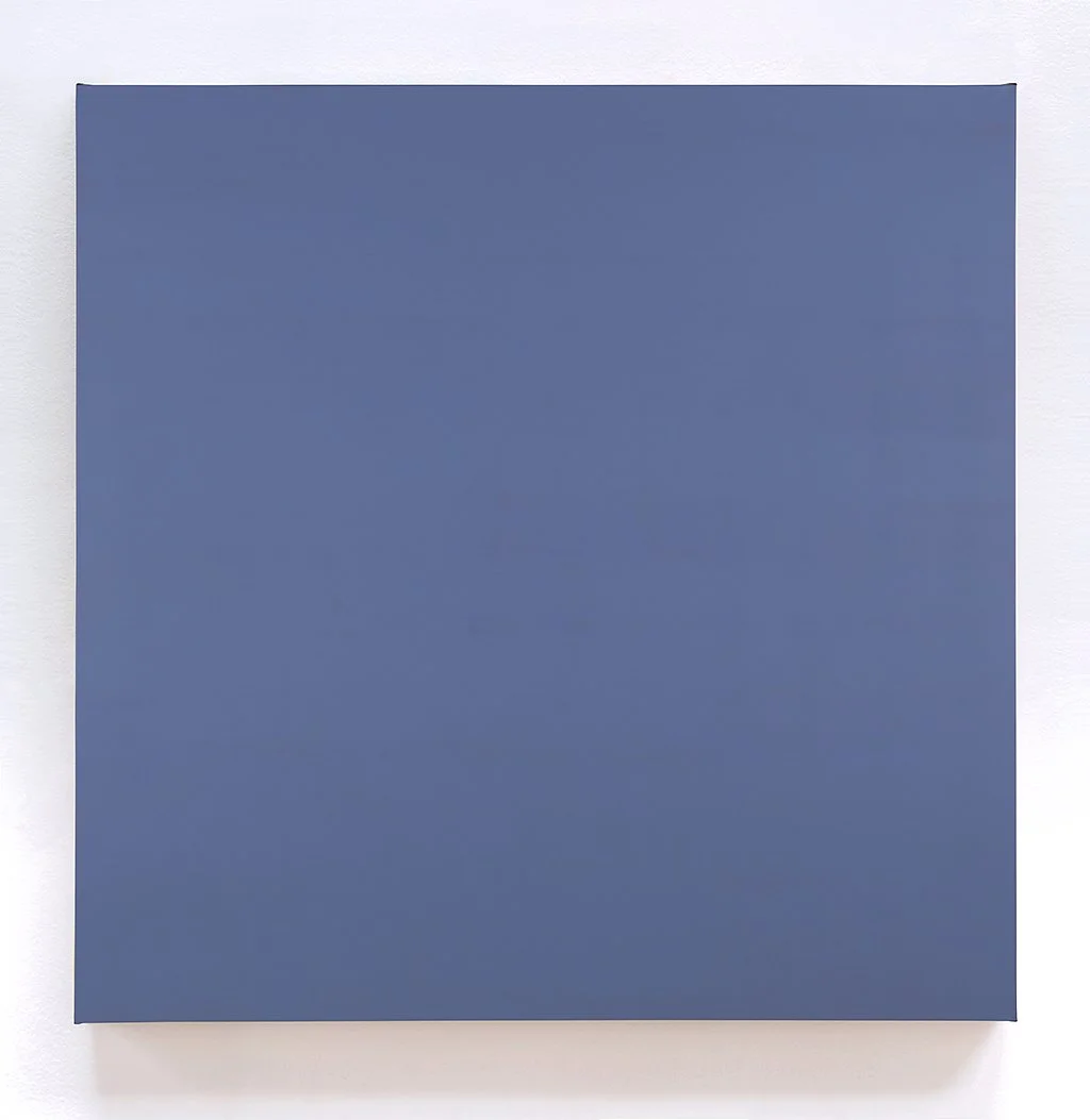 A plain, solid blue square canvas mounted on a white wall.