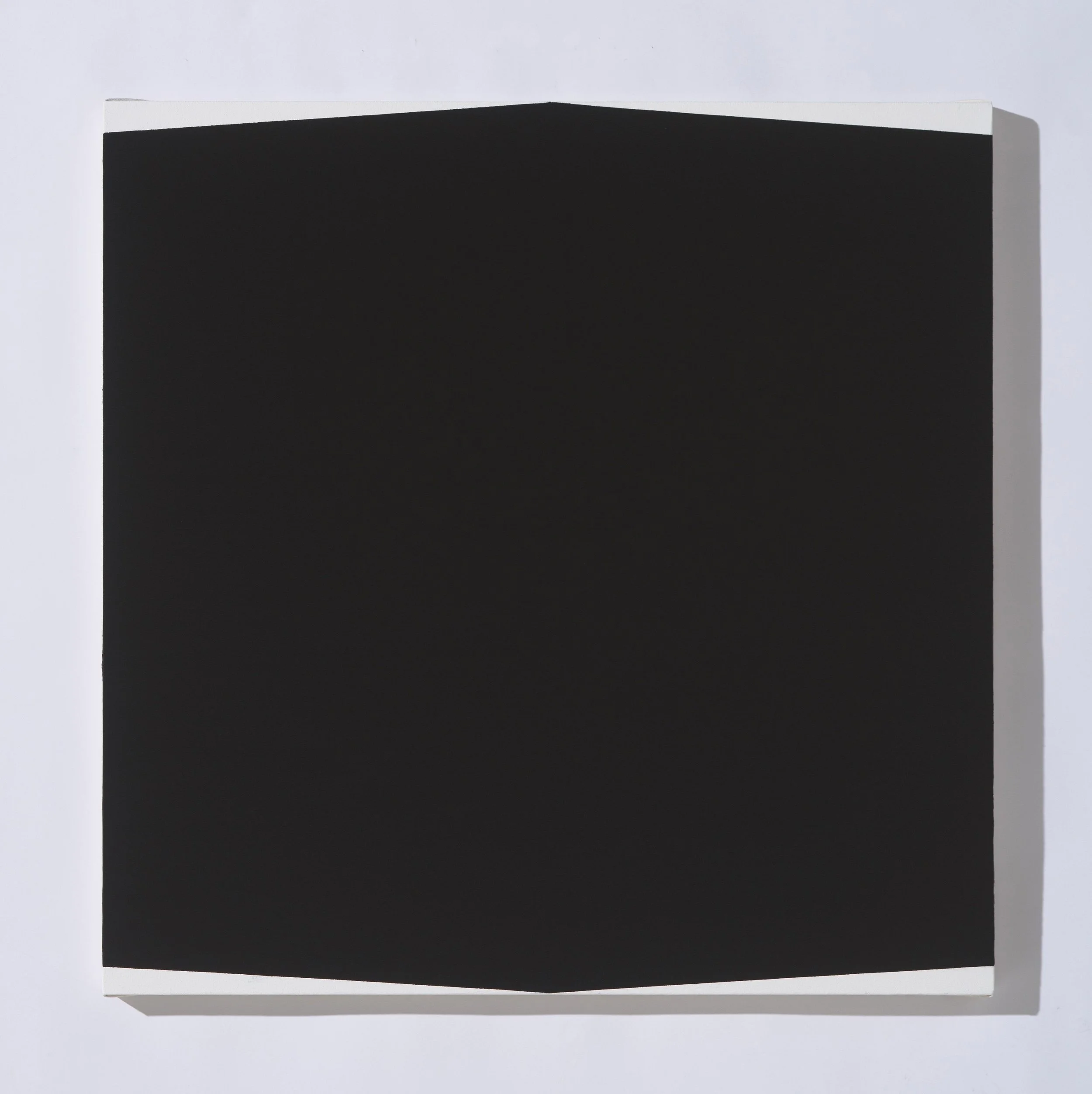 Close-up of a black rectangular object with a white top edge, against a plain white background.