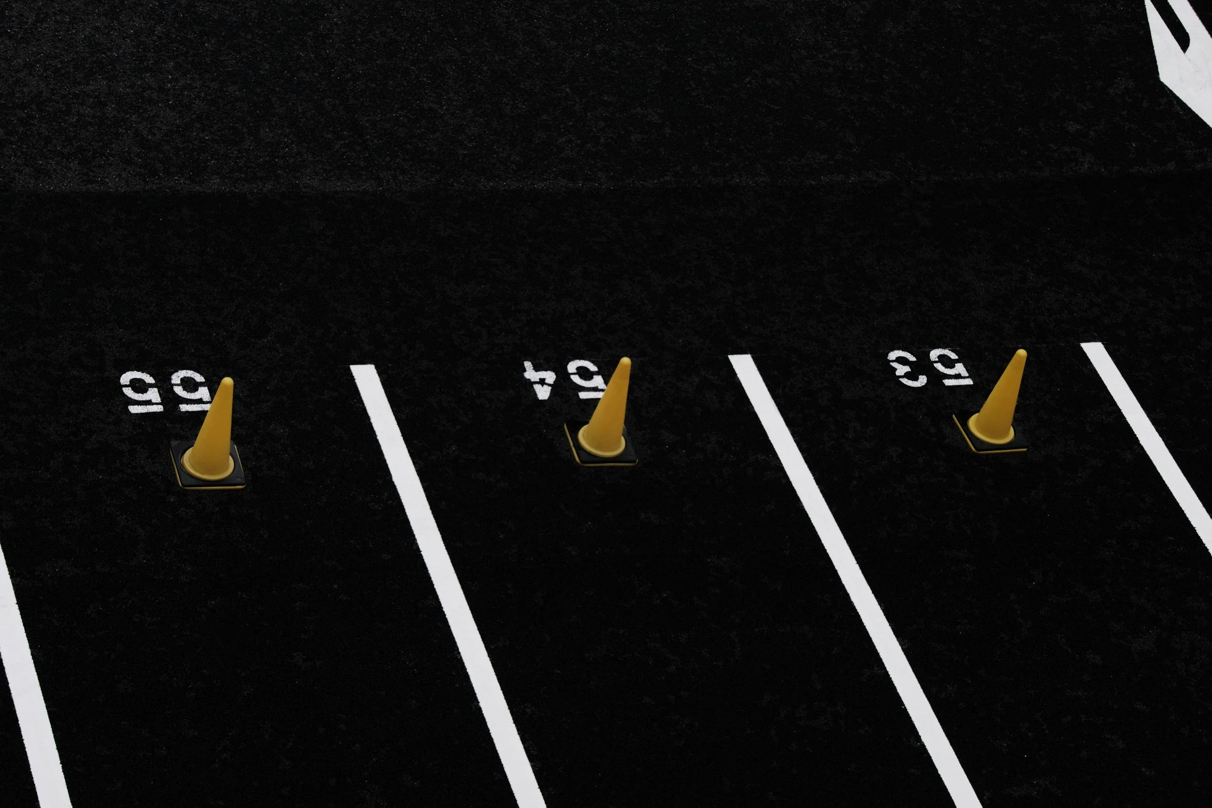 Four numbered parking spots on a black asphalt lot, each marked with white paint and containing yellow traffic cones with black bases.