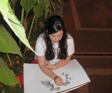 Young woman drawing on a large white sketchpad outdoors at night.