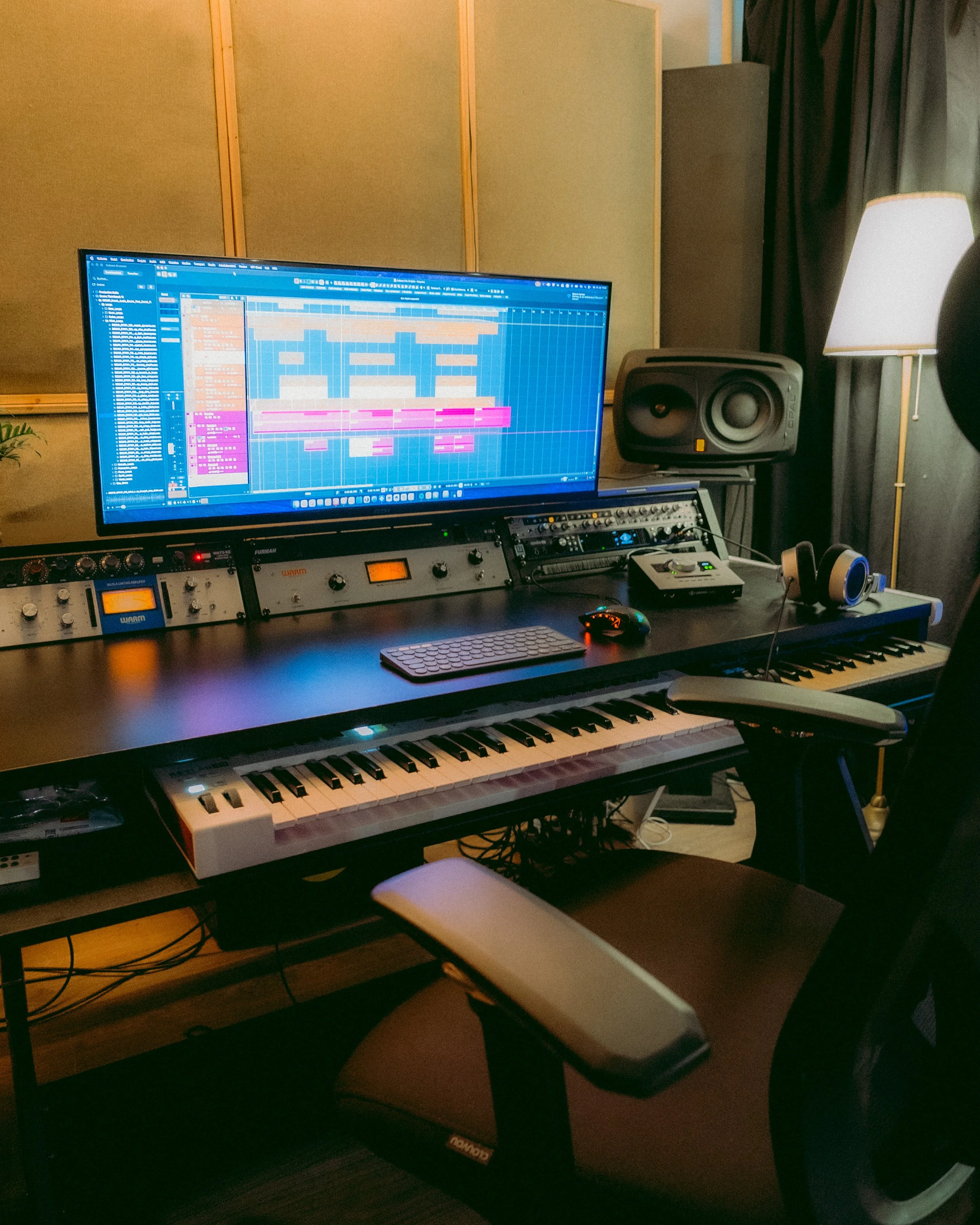 Ein Musikproduktionsstudio mit einem Computermonitor, auf dem eine Digital-Audio-Workstation-Software zu sehen ist, ein Studiomonitor, ein MIDI-Keyboard und Lautsprecherboxen.