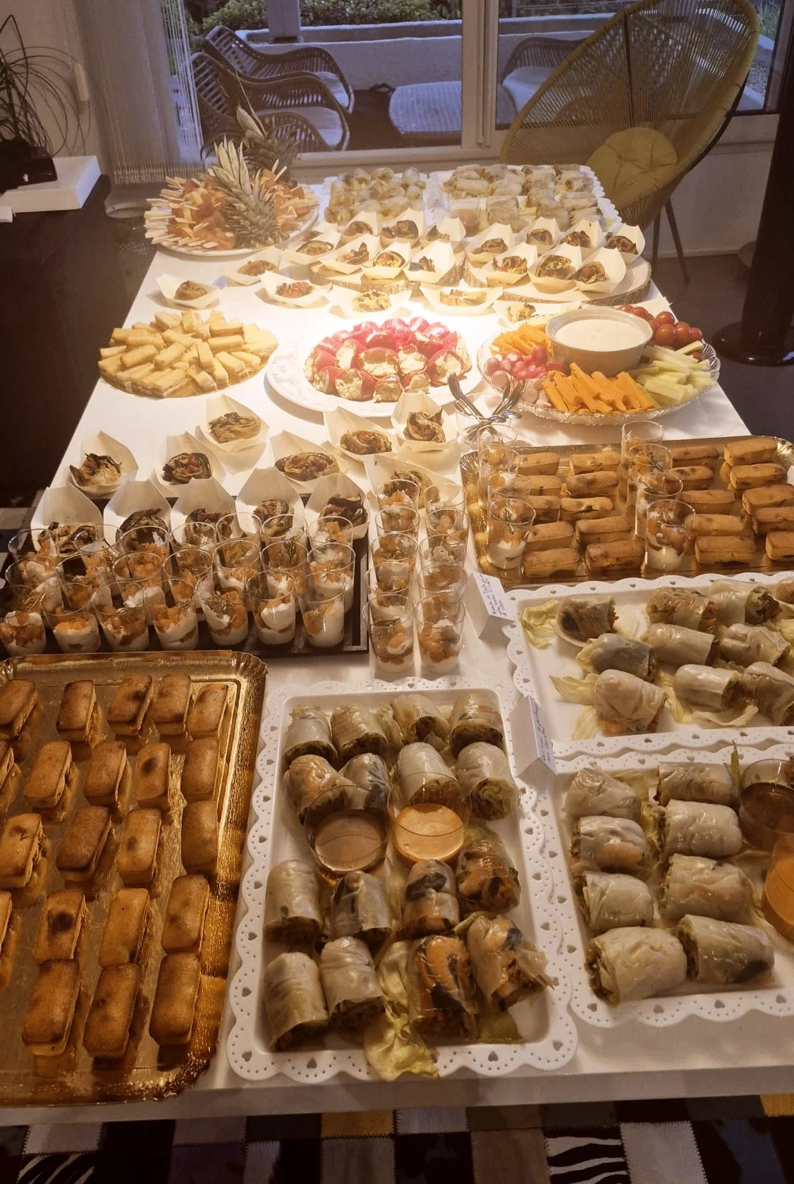 Table dressée avec diverses entrées et desserts, comprenant des rouleaux de printemps, des verrines, des bouchées, des tartes, ainsi que des fruits et un dip.