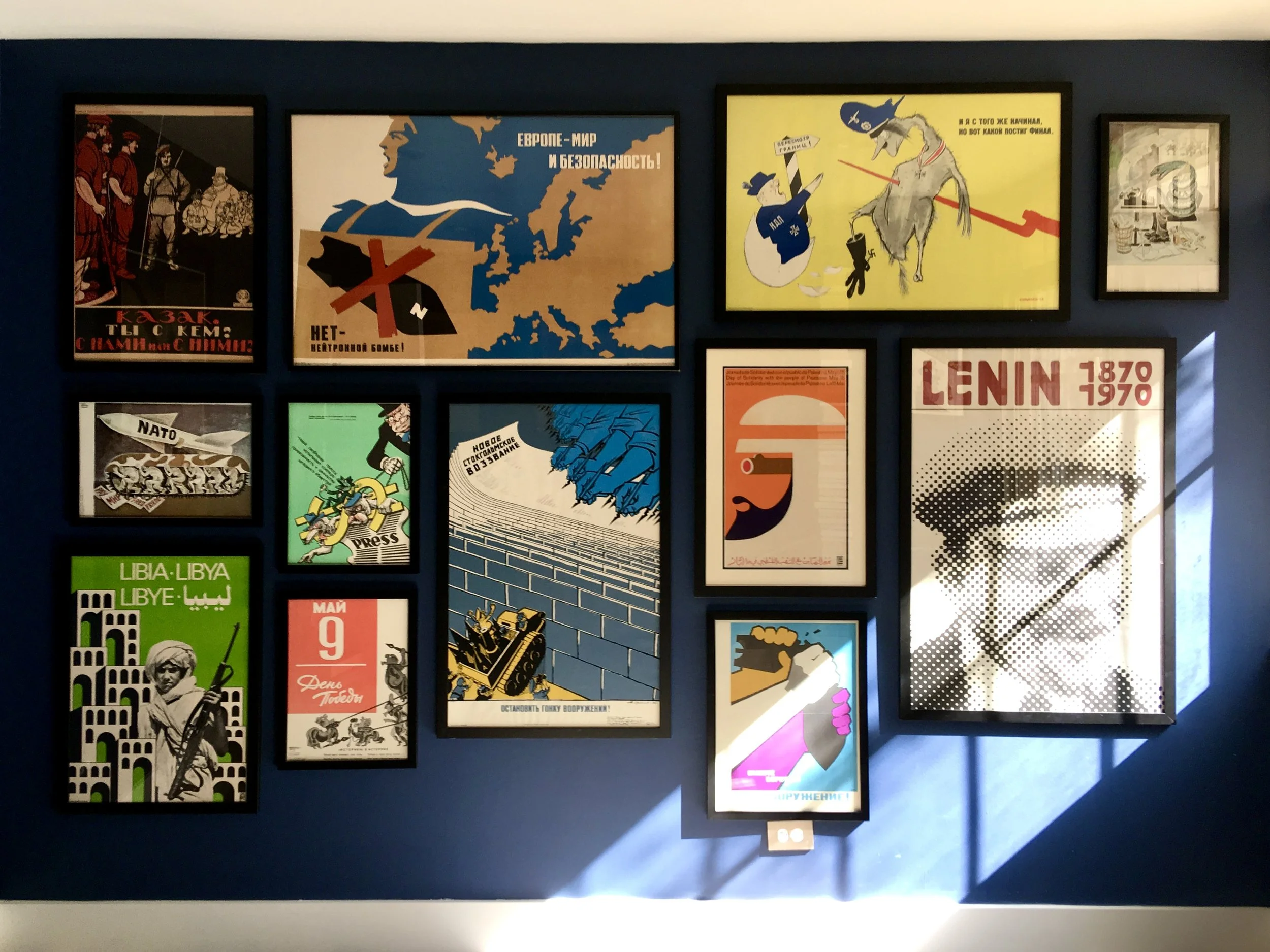 A wall display showing various vintage propaganda posters with themes of war, peace, and political messages in multiple languages including Russian, Arabic, and English.