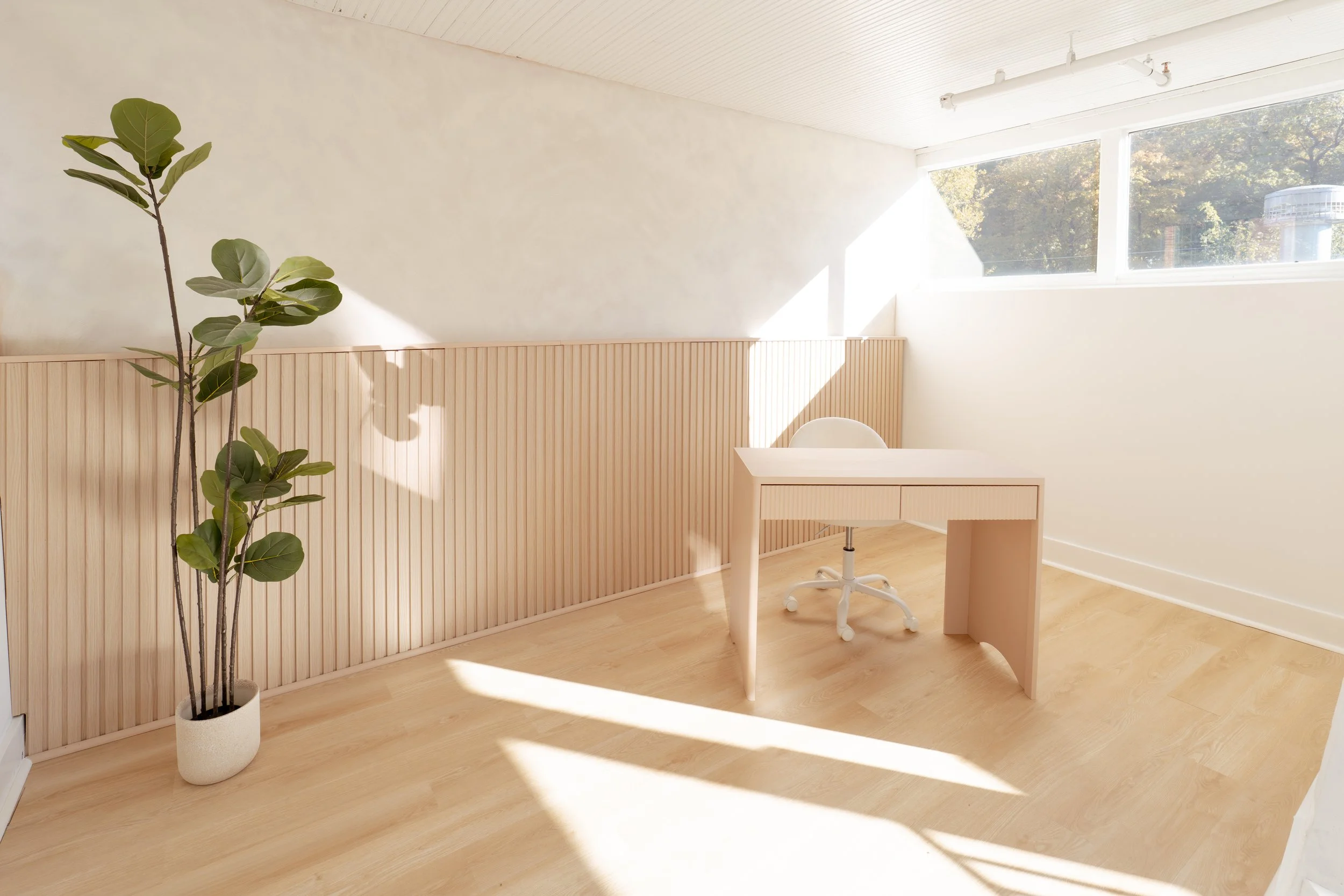 Image of modern desk with white chair next to fiddle leaf plant in lightwashed room.