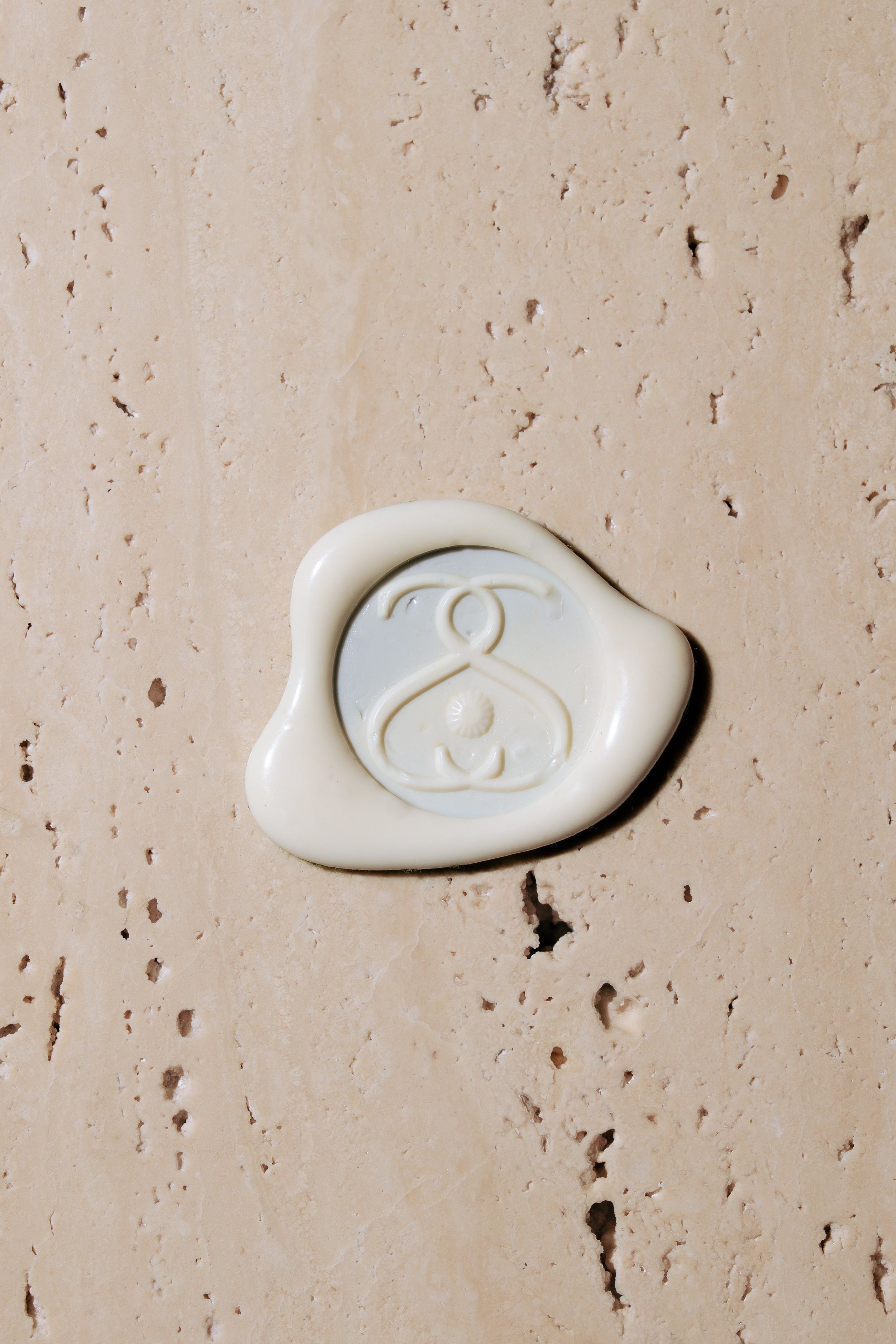 Image of a cream colored wax seal with a logo in the center sitting on top of travertine stone.