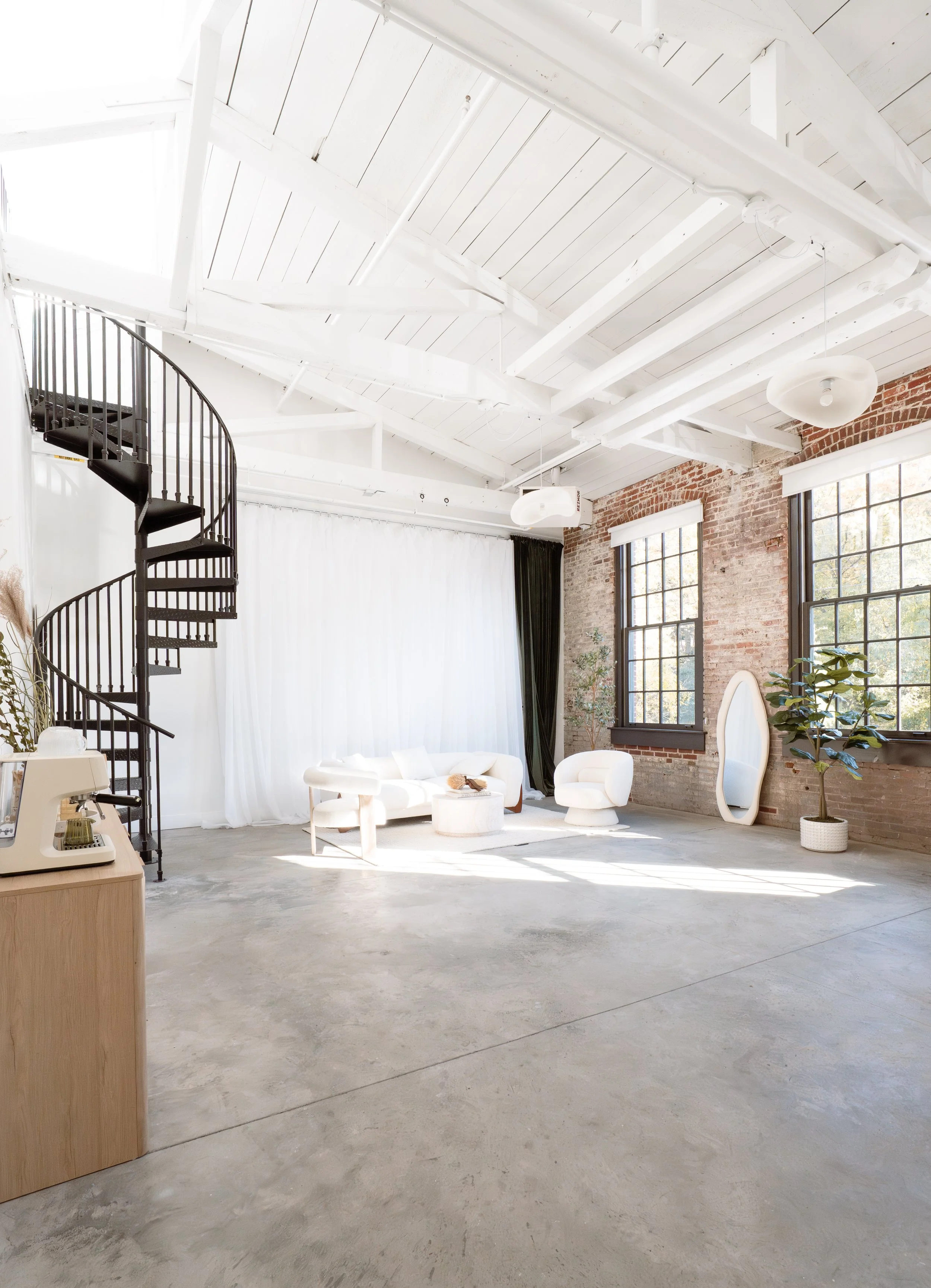 Image of a large natural light photo studio with brick accent walls and high ceilings.