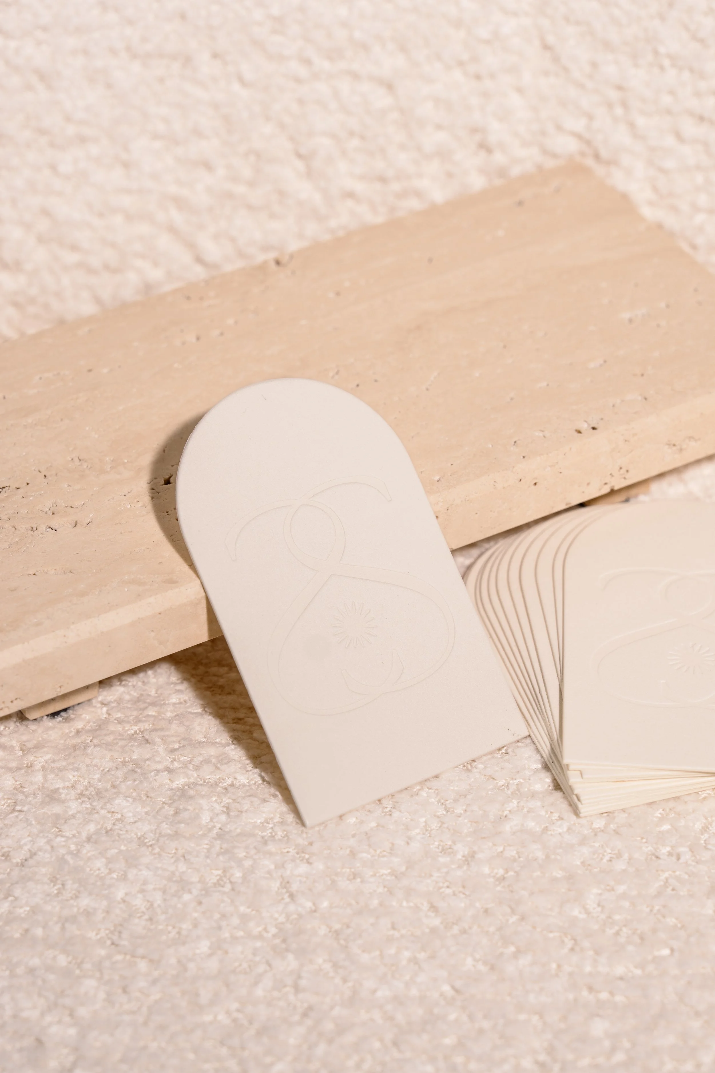 Image of cream colored business cards on top of a travertine tray and cream boucle couch.