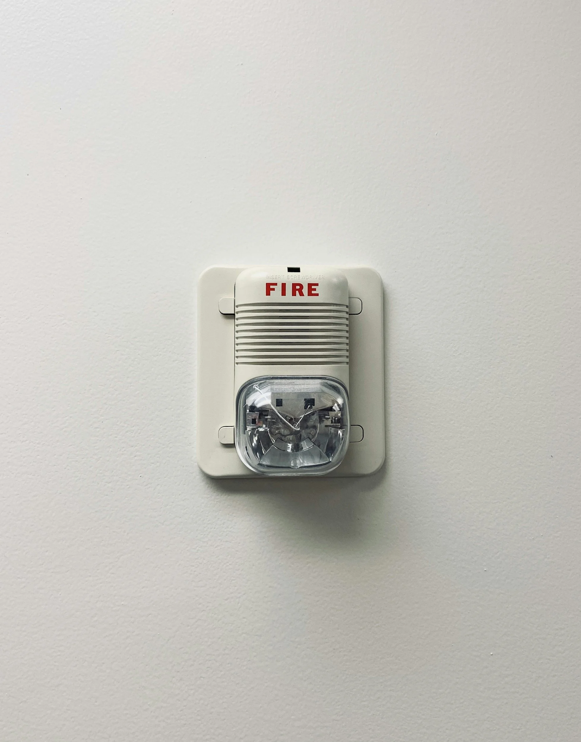 A white smoke detector with a red label that says 'FIRE' on a plain white wall.