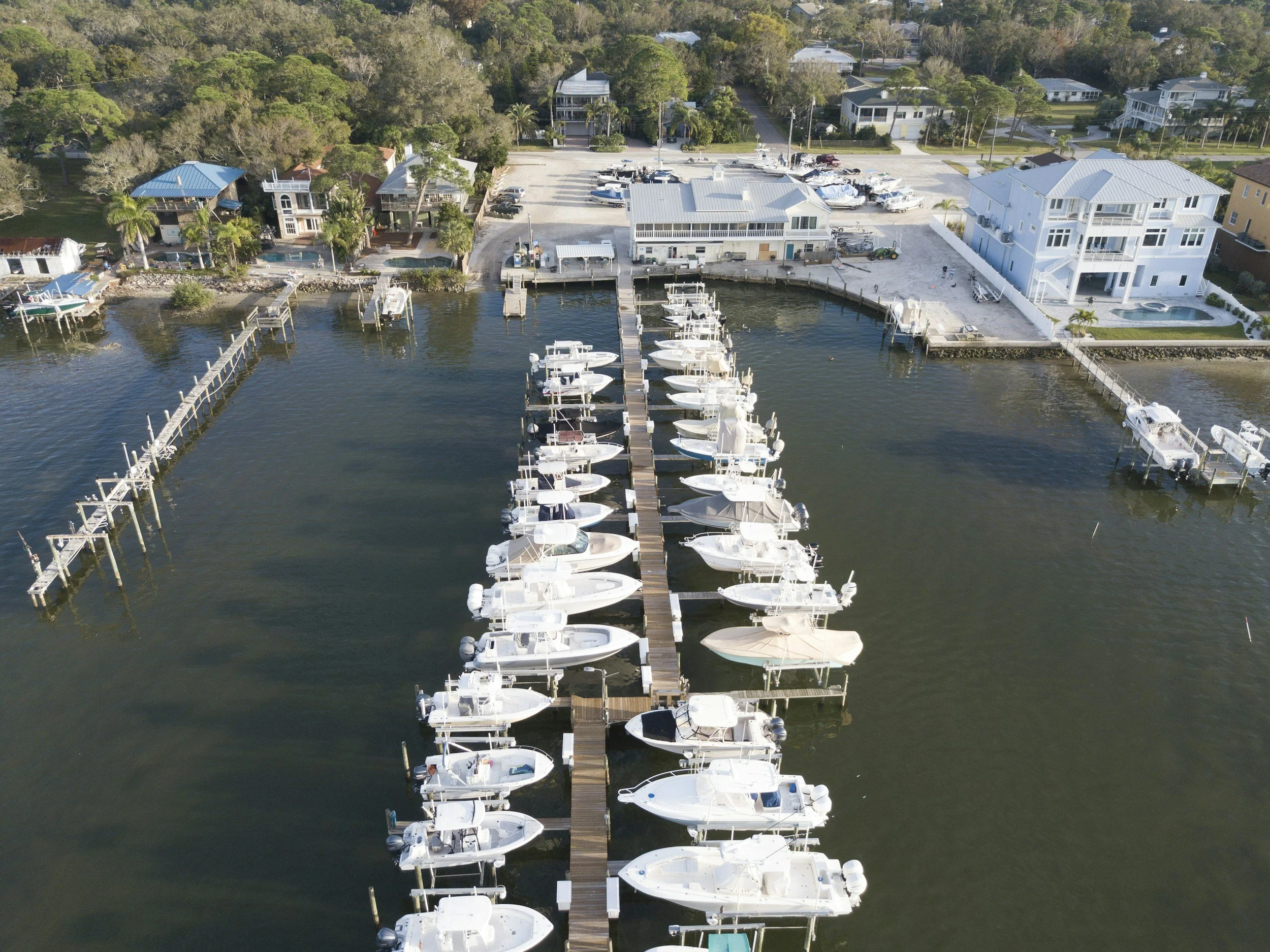 Aerial view of a marina with docked boats, houses, and trees along the waterfront.