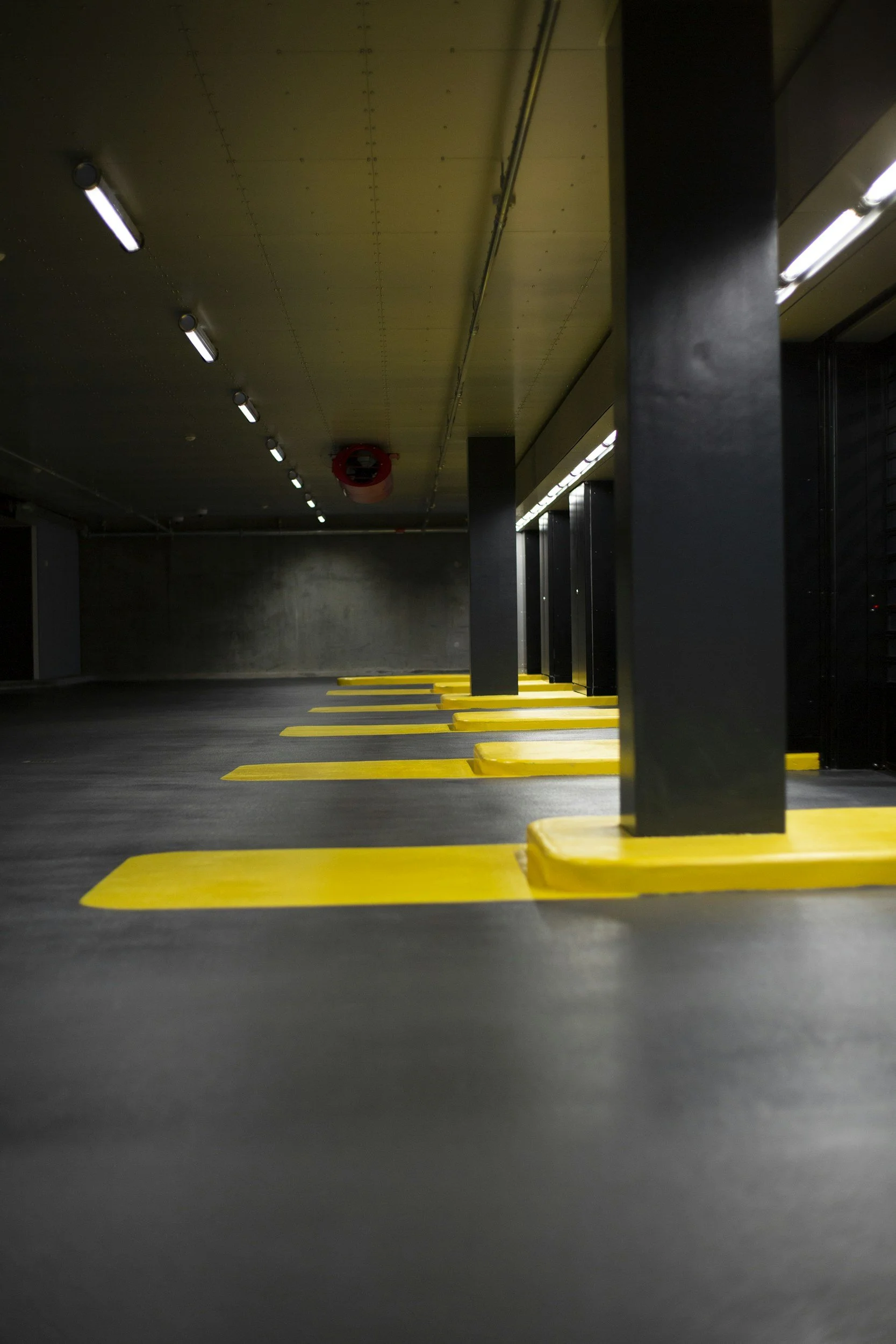 Empty underground parking garage with yellow parking blocks and overhead fluorescent lighting fixtures.