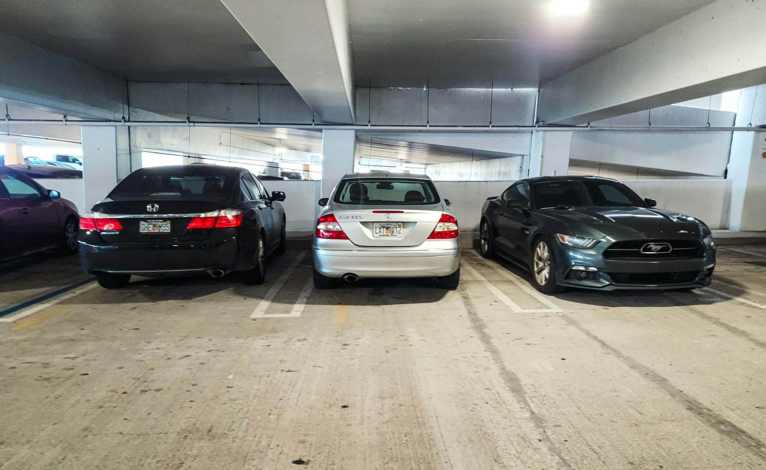 Three cars parked in a parking garage, with concrete ceilings and walls, and a sloped parking ramp in the background.