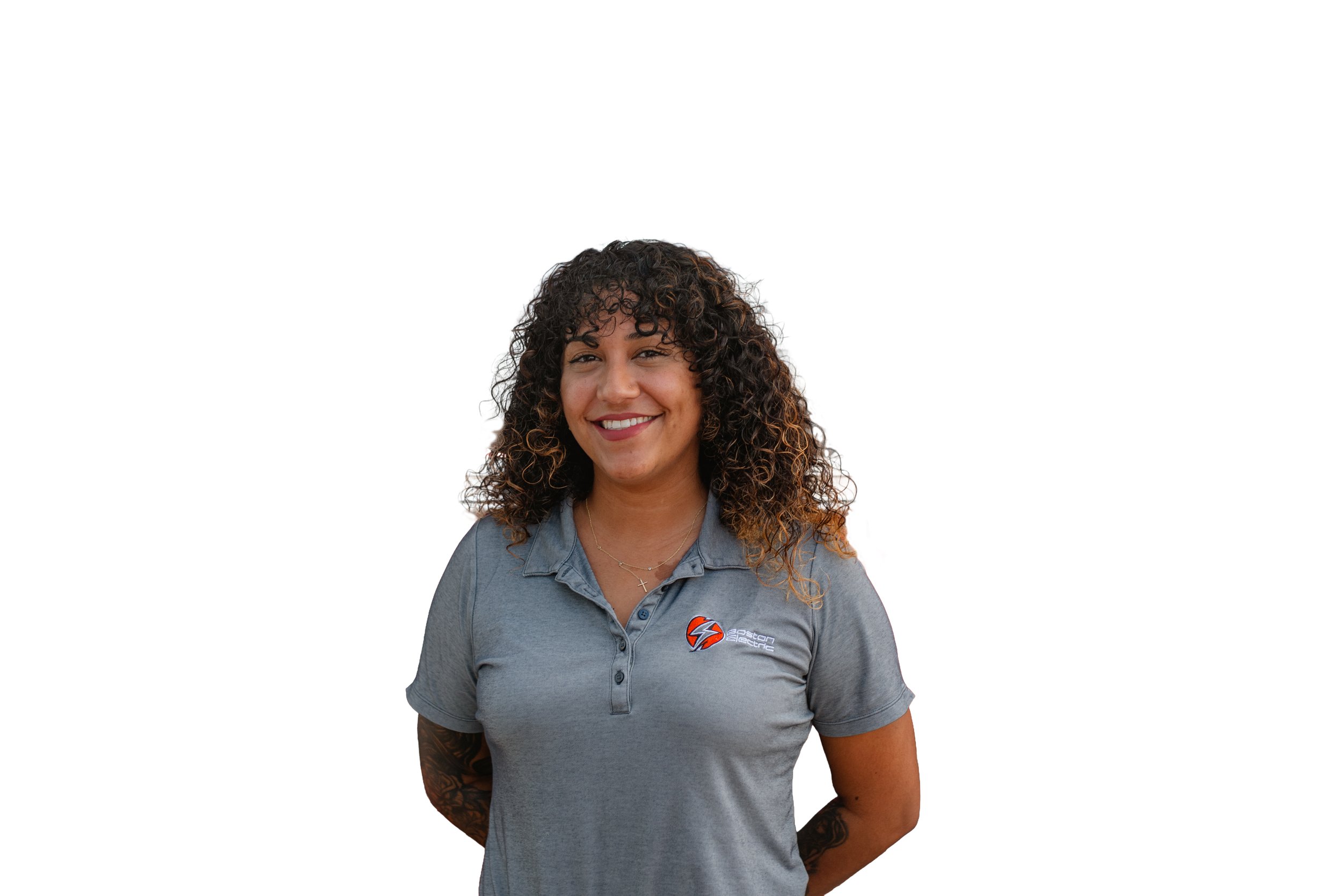 Portrait of a woman with curly hair wearing a grey collared shirt with a logo, smiling against a plain white background.