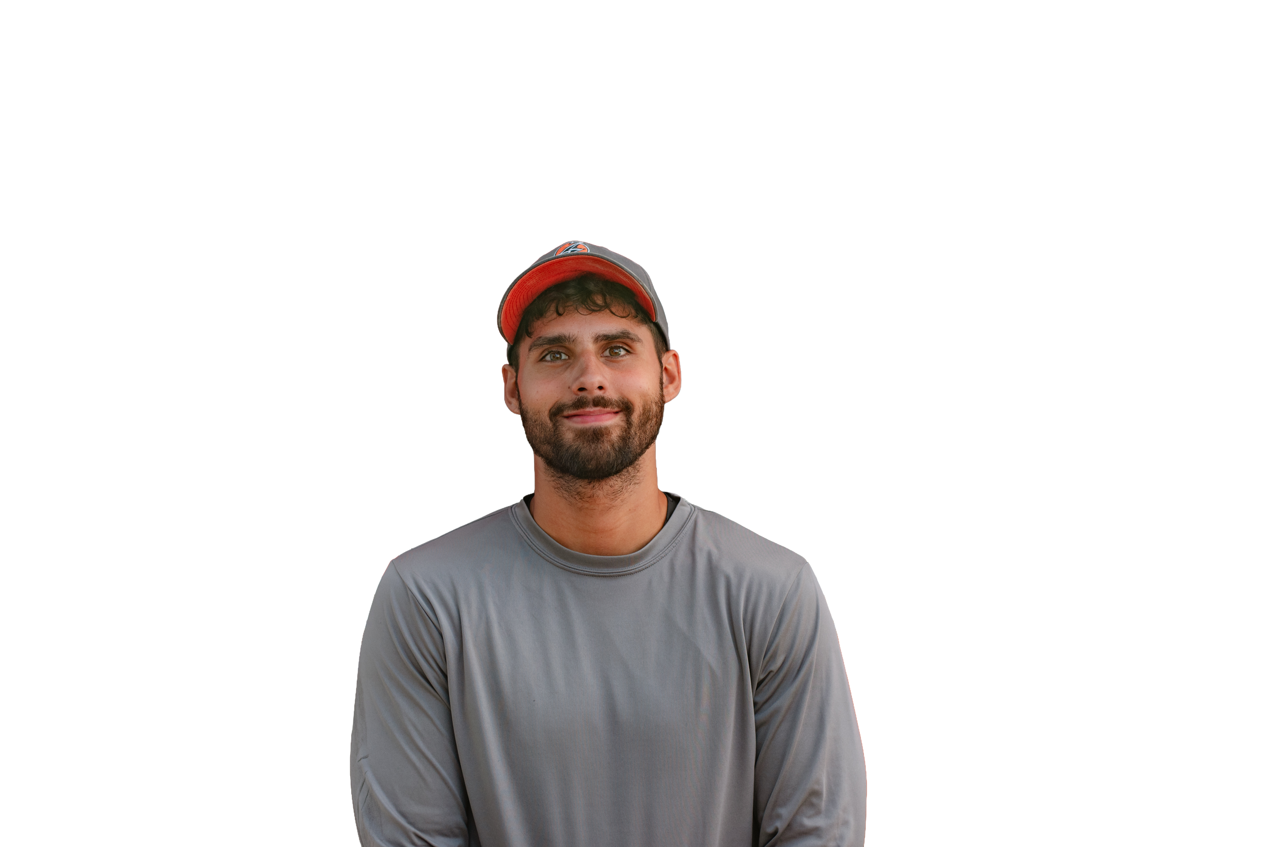A young man with a beard wearing a gray long-sleeve shirt and a red and black baseball cap, smiling and looking at the camera.