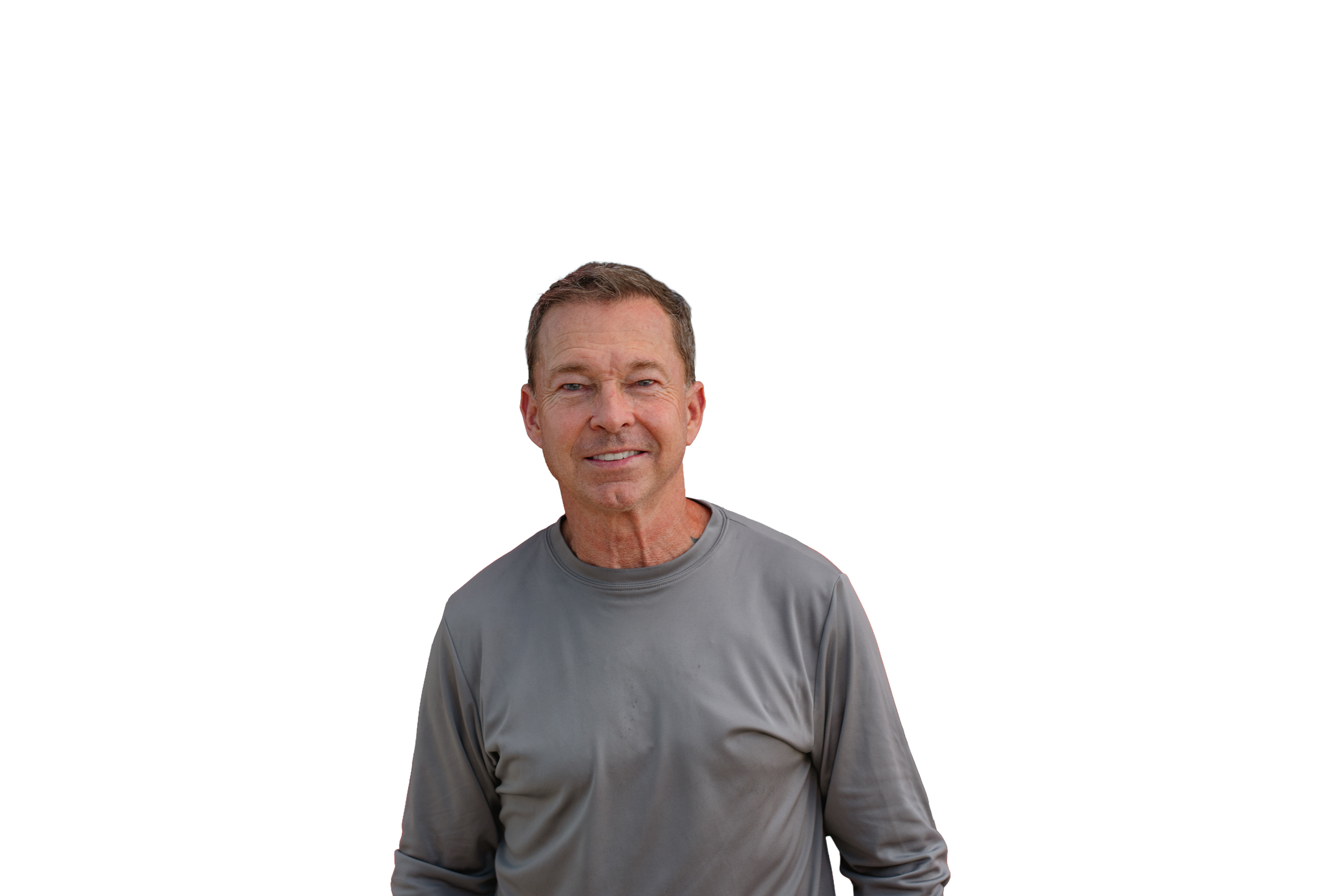 A man with short brown hair and blue eyes smiling, wearing a gray long-sleeve shirt, standing against a plain white background.