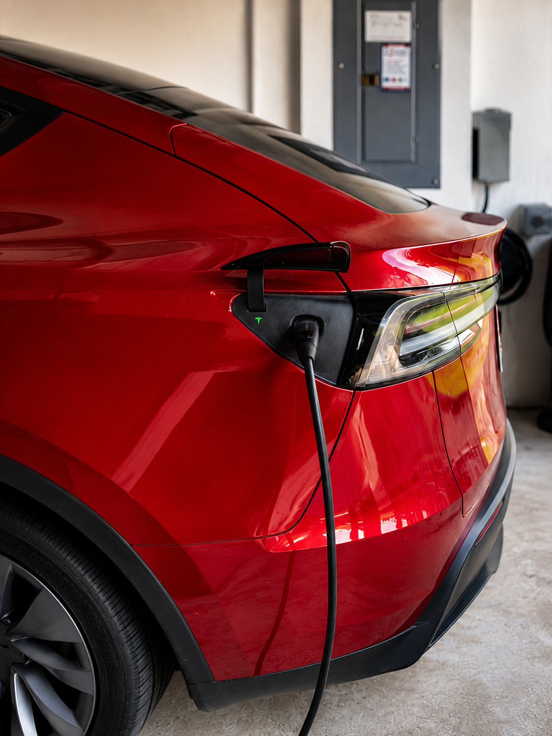 Red electric car being charged in a garage with charging cable connected to the rear side.
