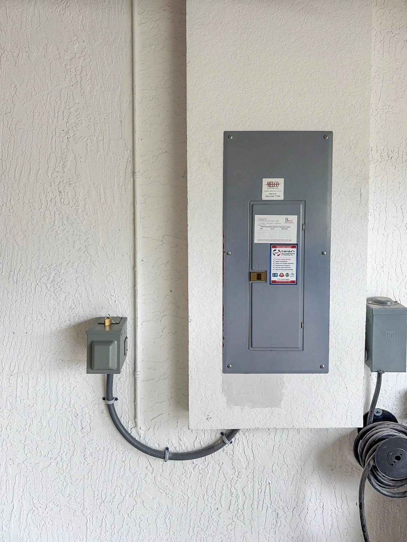 Electrical panel on a textured white wall with electrical boxes and cables.