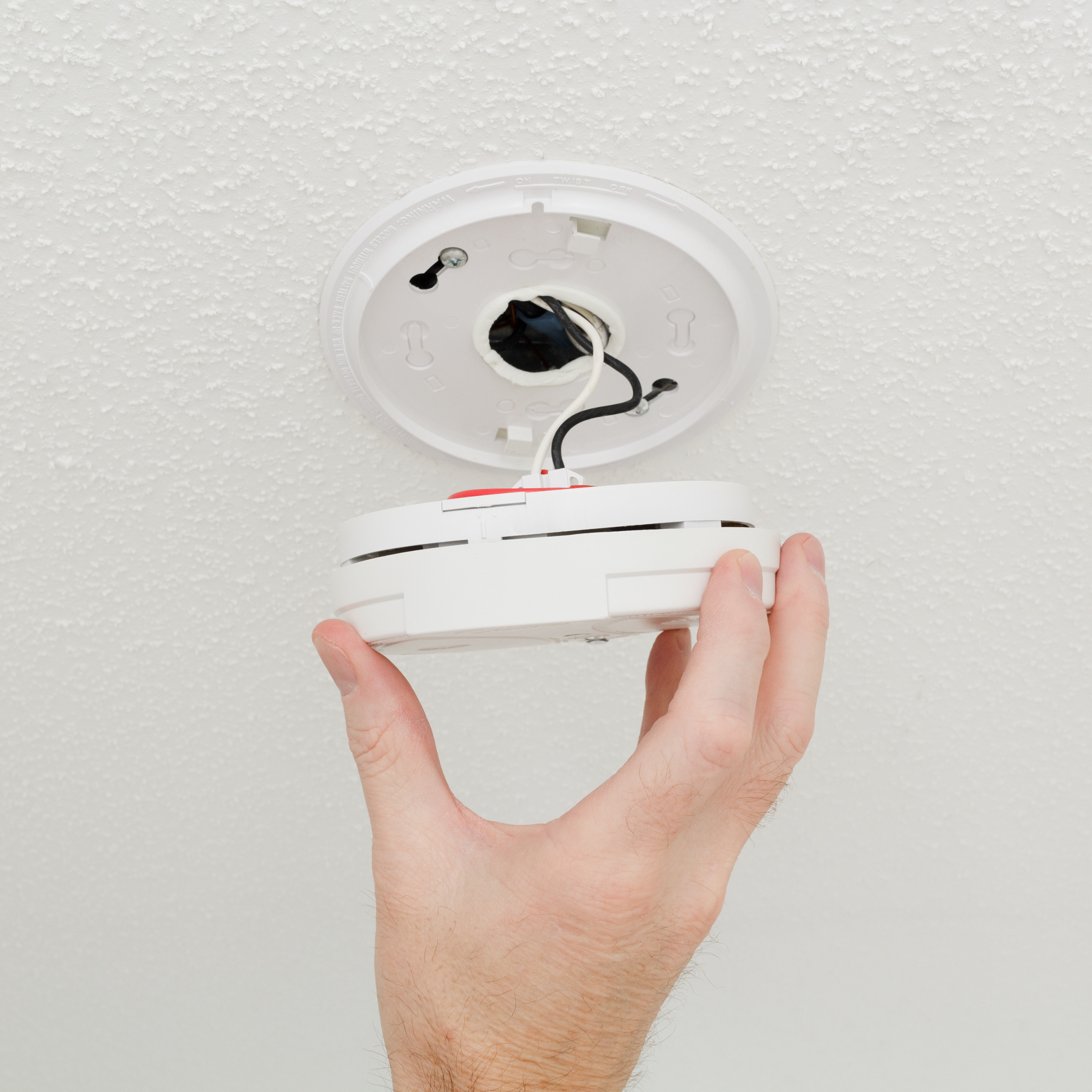 A white smoke detector with a red label that says 'FIRE' on a plain white wall.