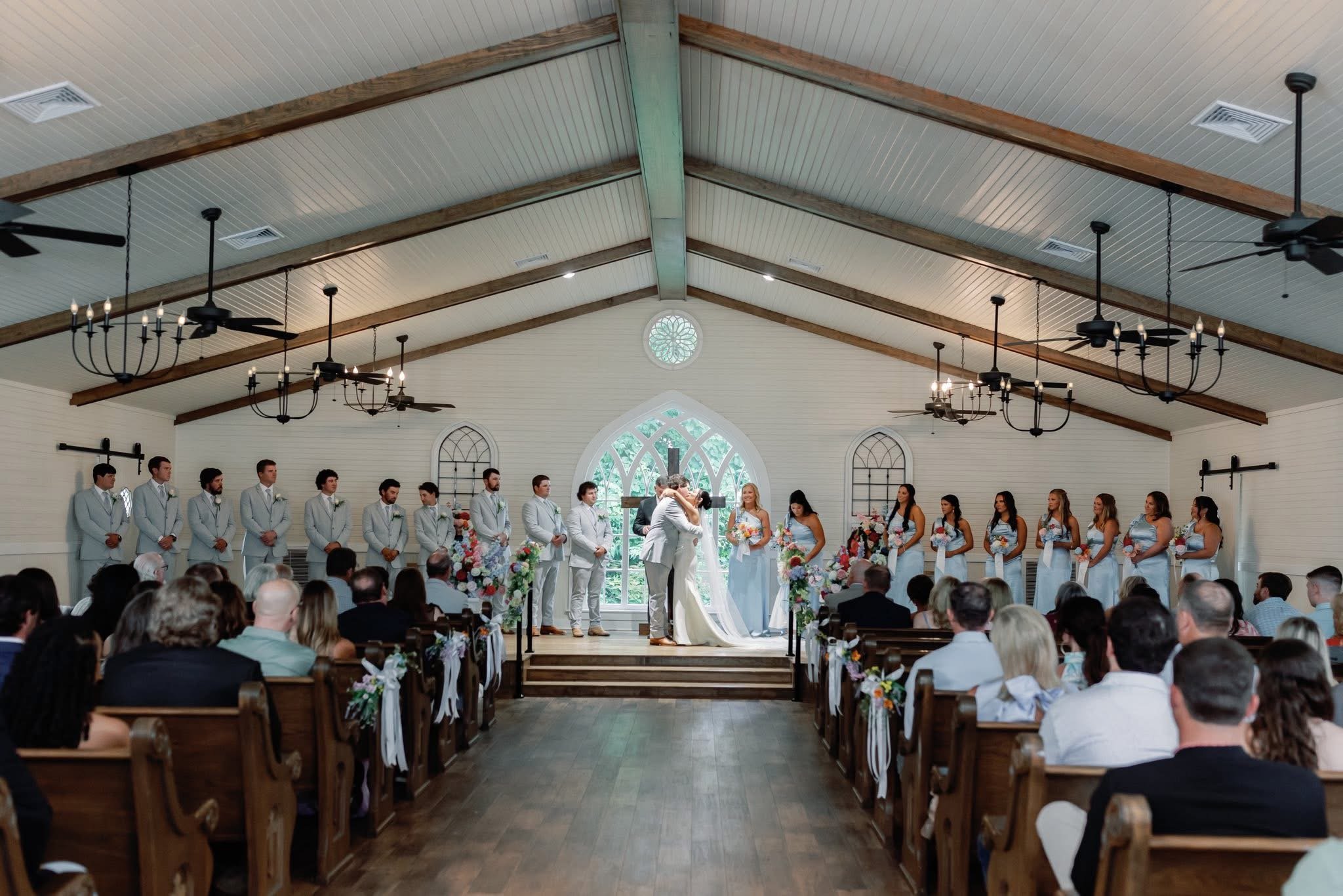 A wedding ceremony inside a church, with the officiant and couple in the center, surrounded by bridesmaids and groomsmen, with guests seated facing the altar.