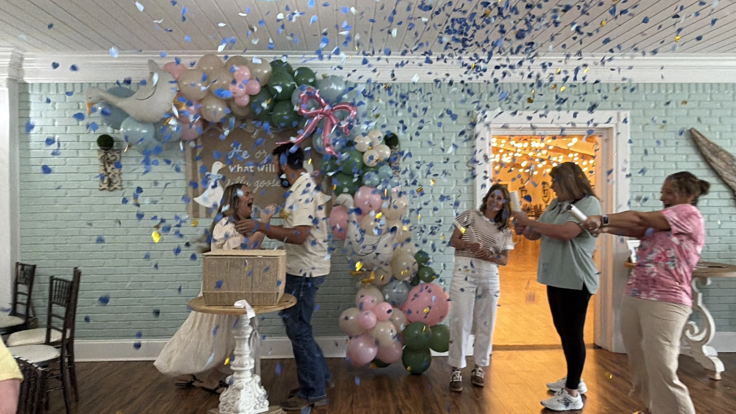 People celebrating a balloon party with blue, pink, and green balloons, and confetti falling from above.