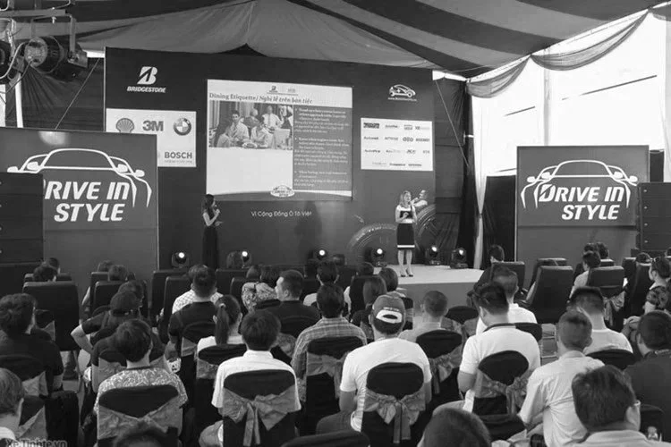 Indoor event with a large audience seated in front of a stage displaying