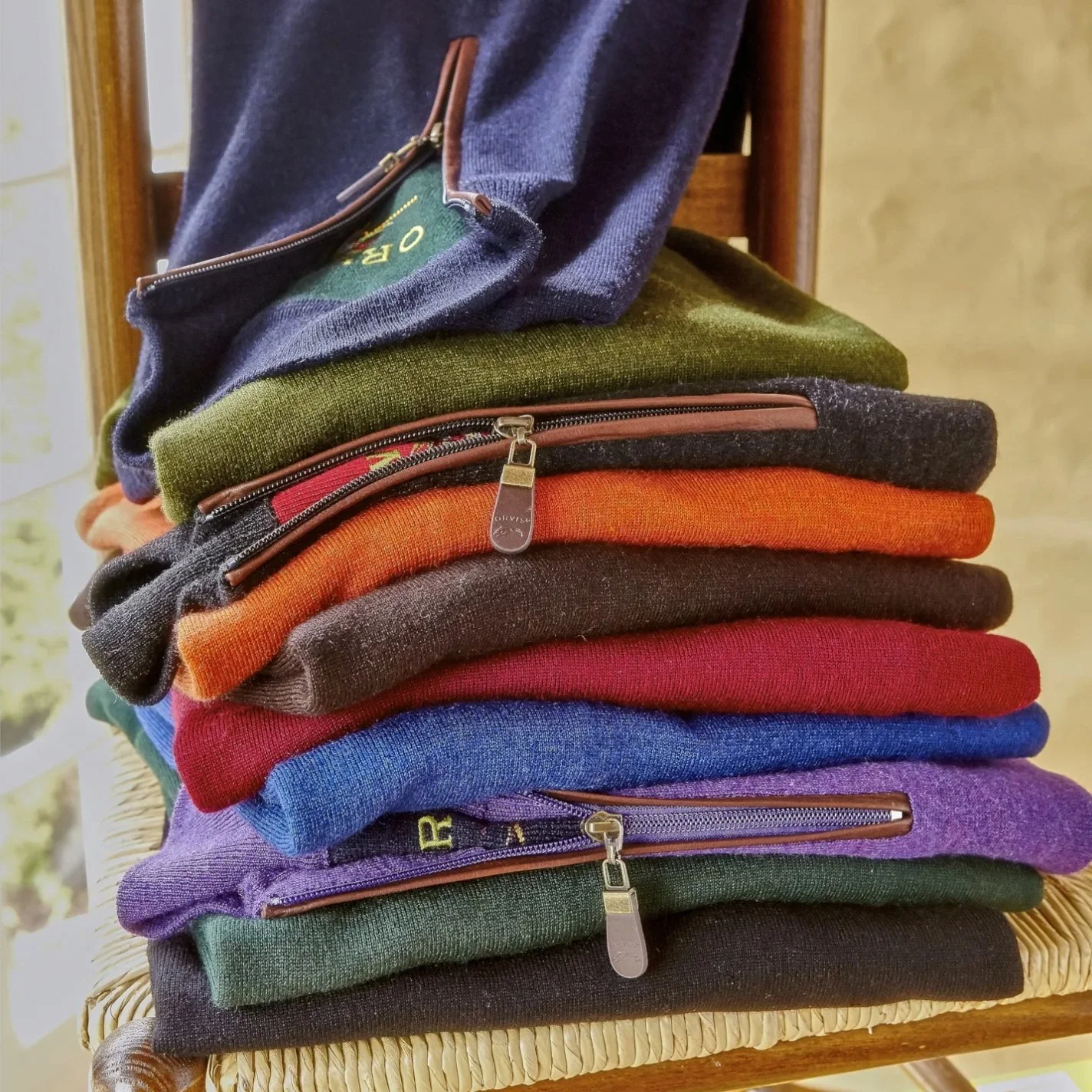 A stack of folded colorful sweatshirts with visible zippers, placed on a woven chair.
