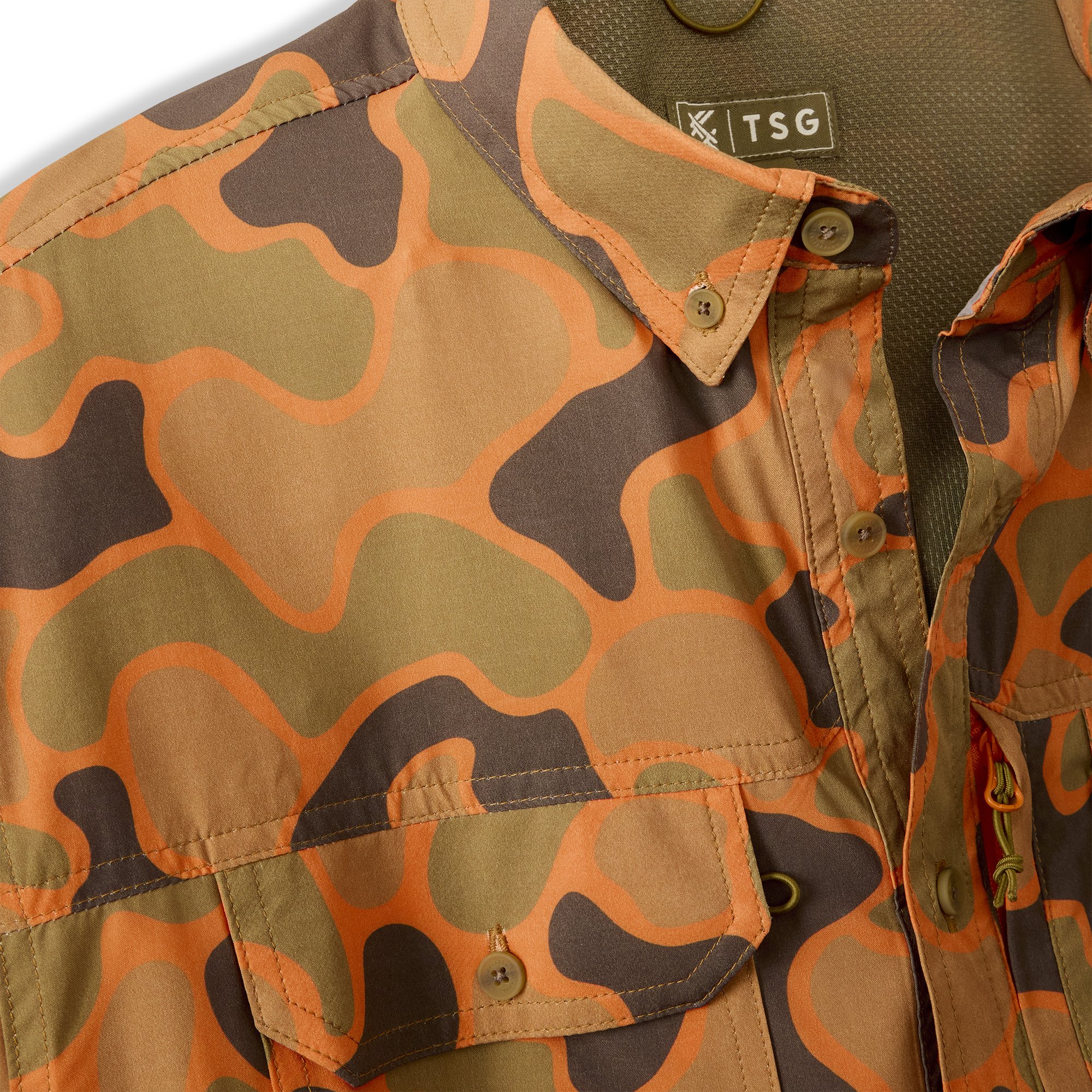 Close-up of a camo patterned button-up shirt with orange, green, and black patches, showing collar, buttons, and a TSG label.