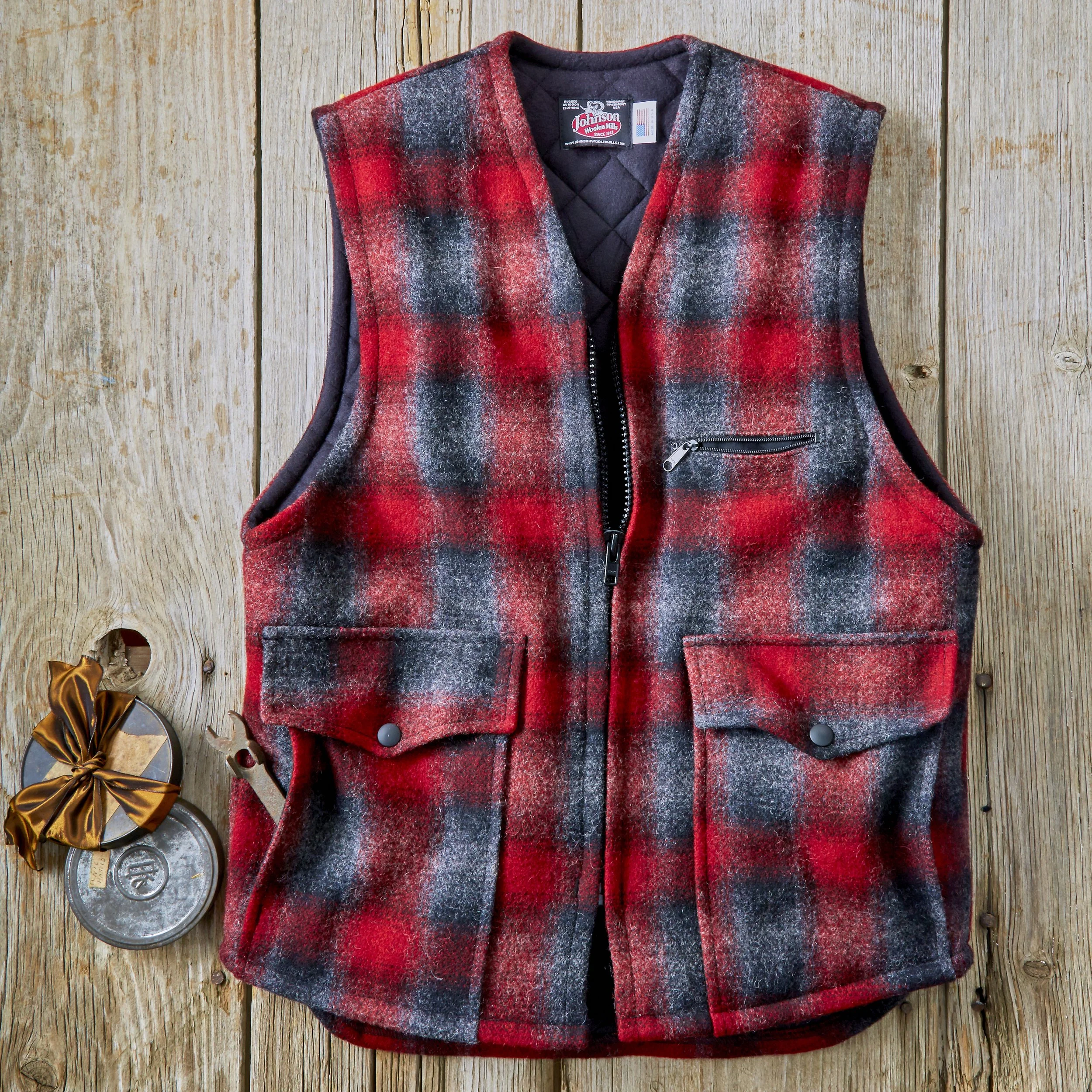 A red, black, and grey plaid sleeveless vest with a zipper and a small pocket, hanging on a wooden wall.