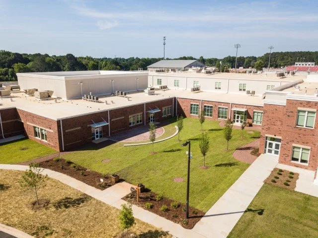 Aerial view of a modern school building with a grassy courtyard, small trees, walkways, and surrounding landscape.