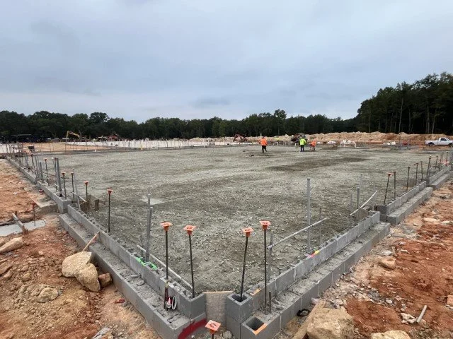 Construction site with concrete foundation, rebar, and construction workers in the background.