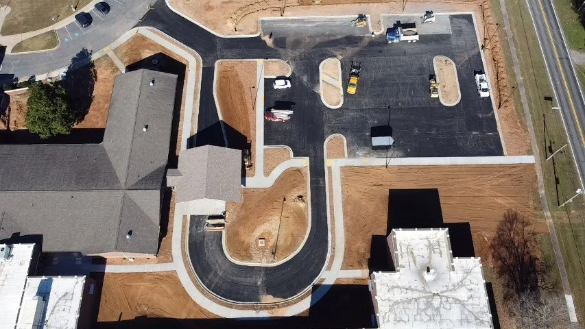 Aerial view of a parking lot and building, with surrounding roads and landscaping.
