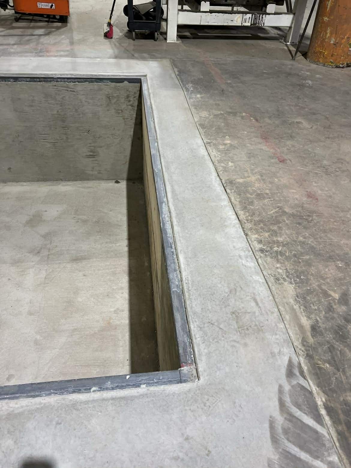 Concrete floor with a square hole, partially constructed, with metal framing along the edges in an industrial or construction setting.