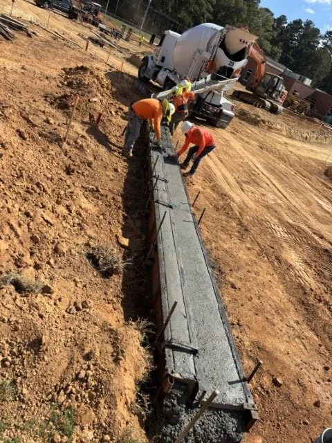 Construction workers pouring concrete into a long formwork on a building site.