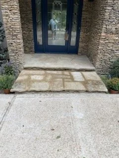 Stone pathway leading to a blue door with glass panels, flanked by brick walls and small potted plants.