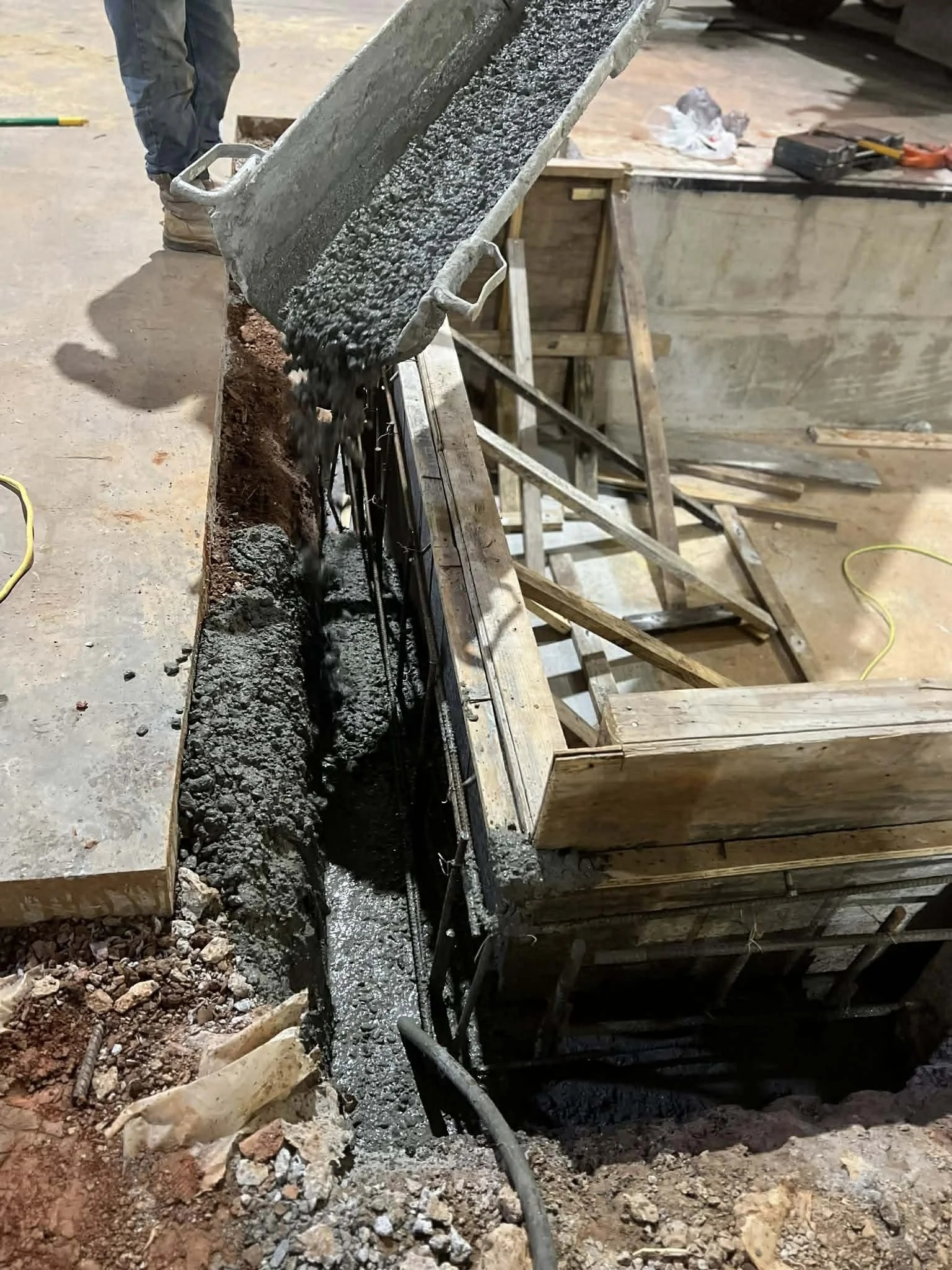 Concrete being poured into a wooden form for a foundation at a construction site.