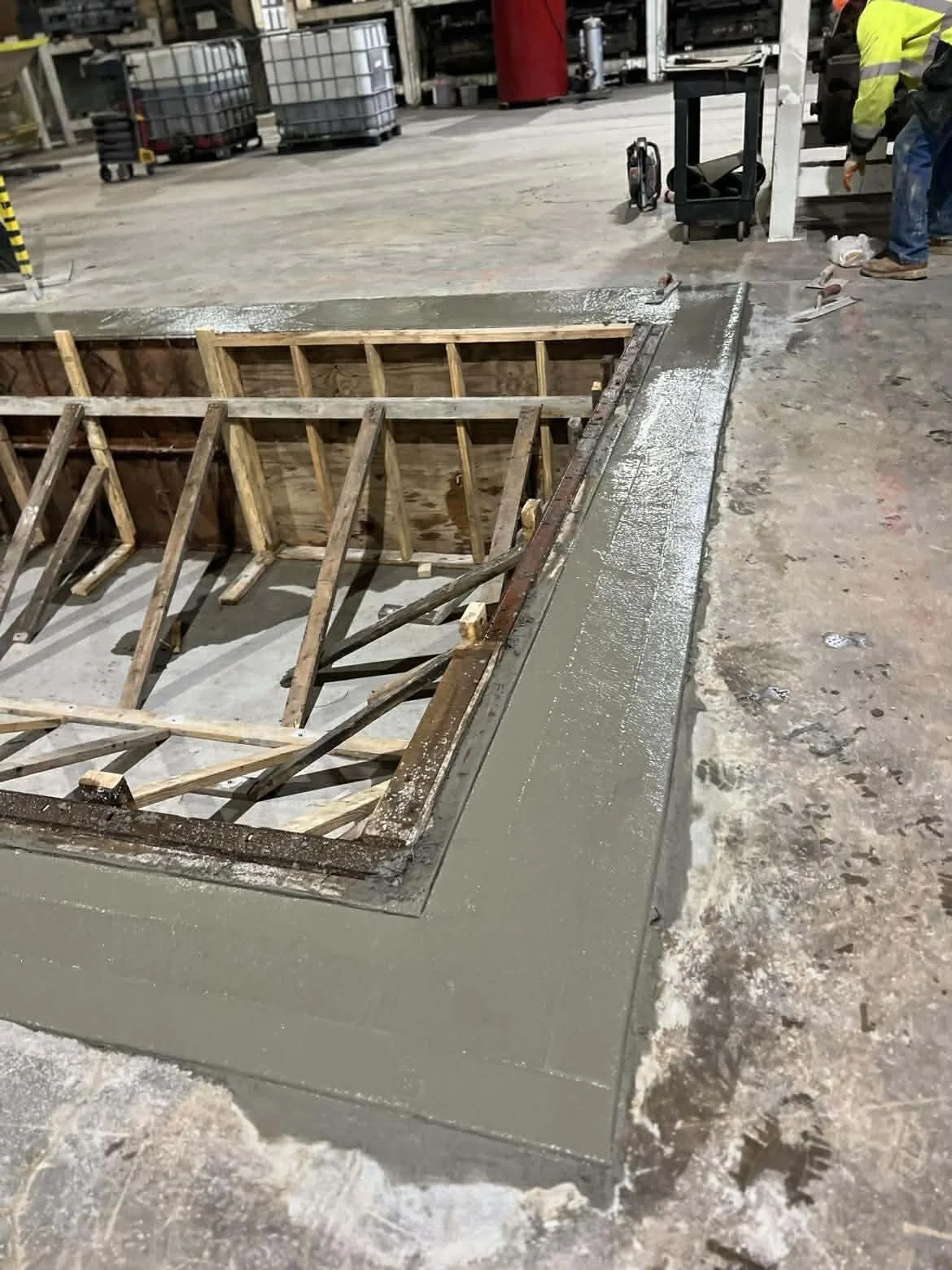 Construction site showing concrete and rebar frame for a new floor or platform, with workers and construction tools in the background.