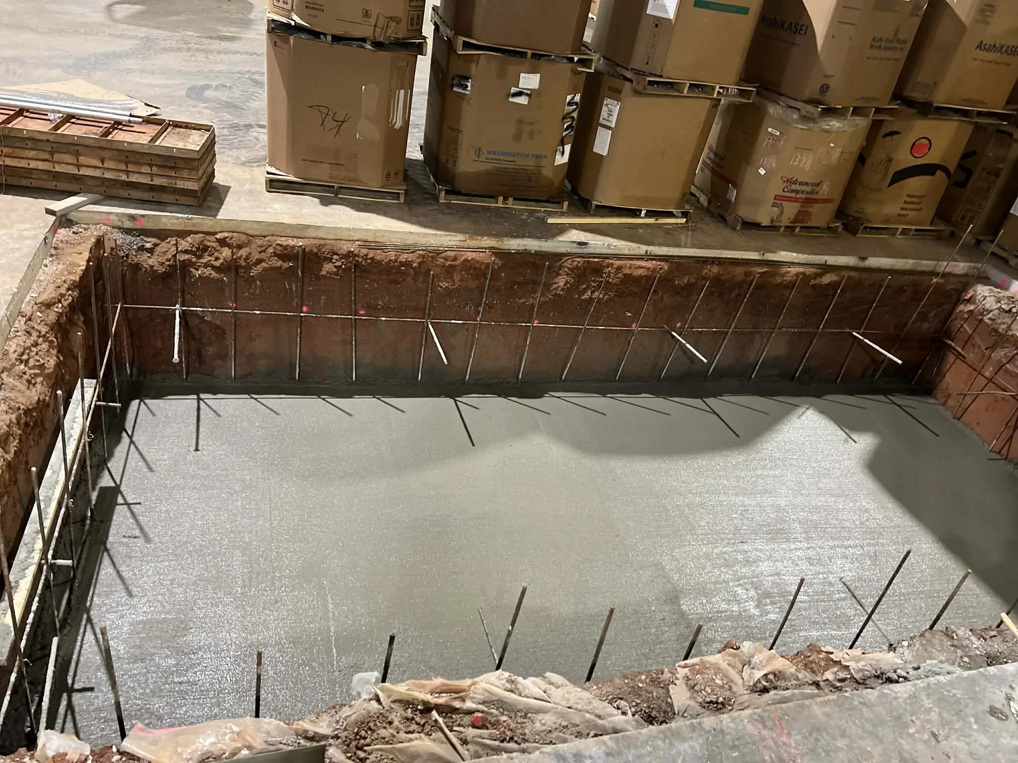 A construction site with an excavated area and freshly poured concrete on the ground, surrounded by metal rebar for reinforcement.