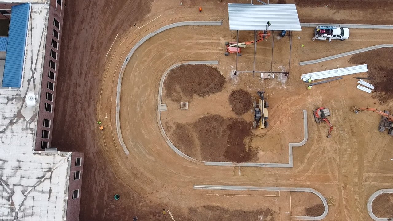 An aerial view of a construction site with dirt pathways, construction vehicles, a small building with a roof, and construction workers.