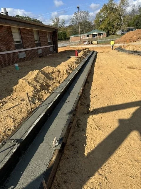 Construction site with a foundation or footing being poured for a building, with some rebar, zigzagging along the ground.