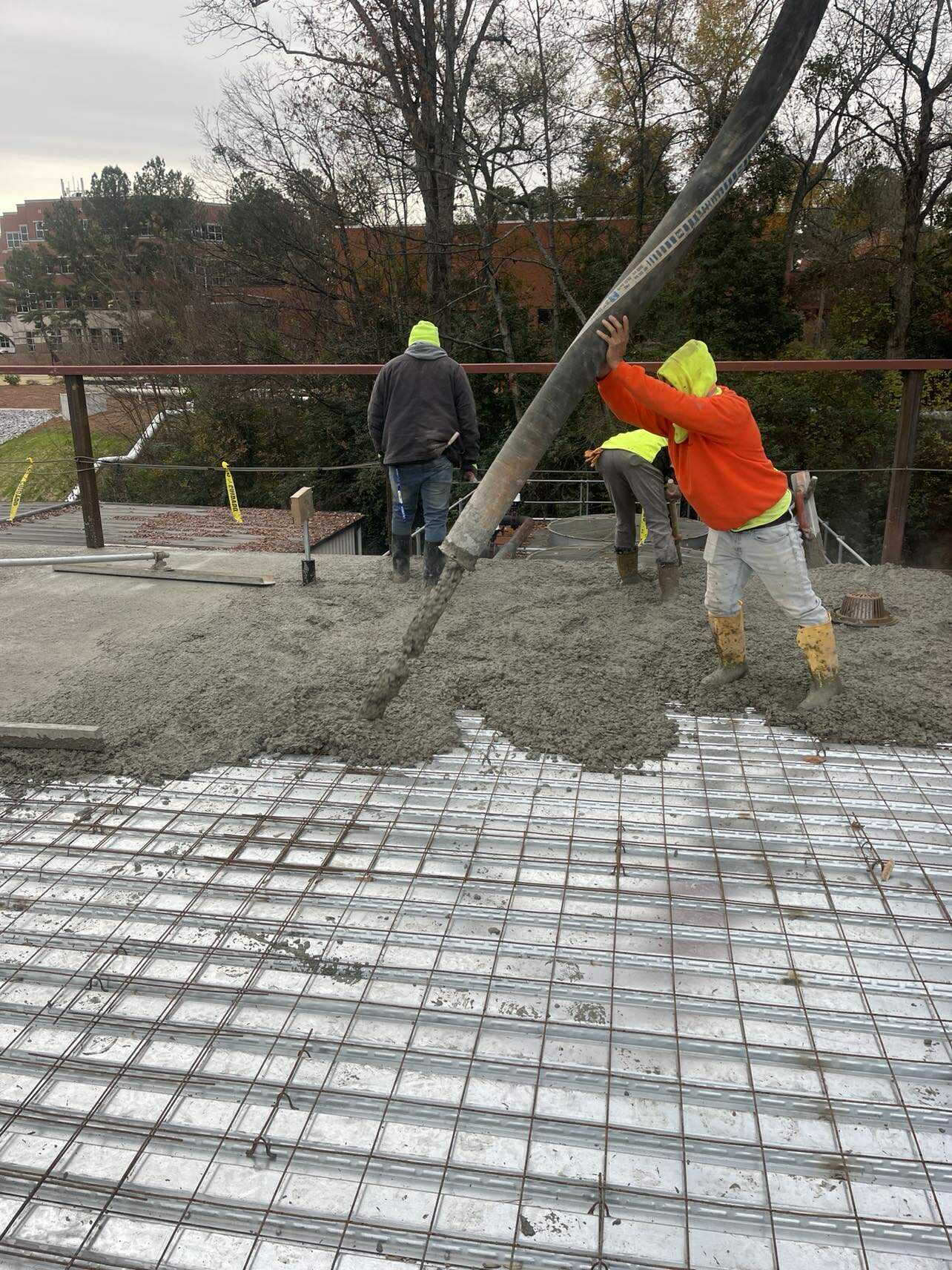 Construction workers pouring concrete over rebar grid on a building site during daytime.